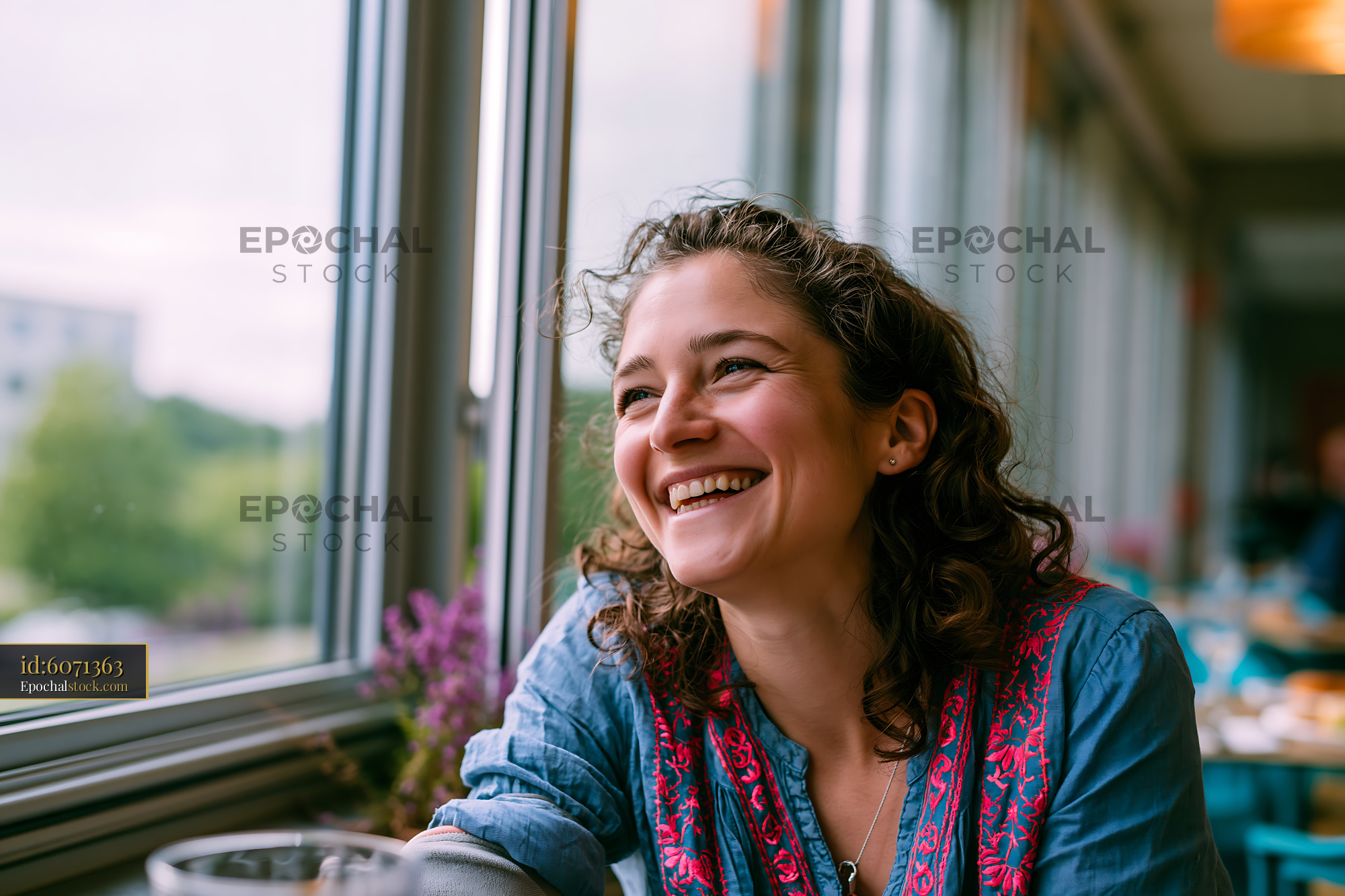 Watermarked full-resolution preview of Woman smiling by a large window in a cafe