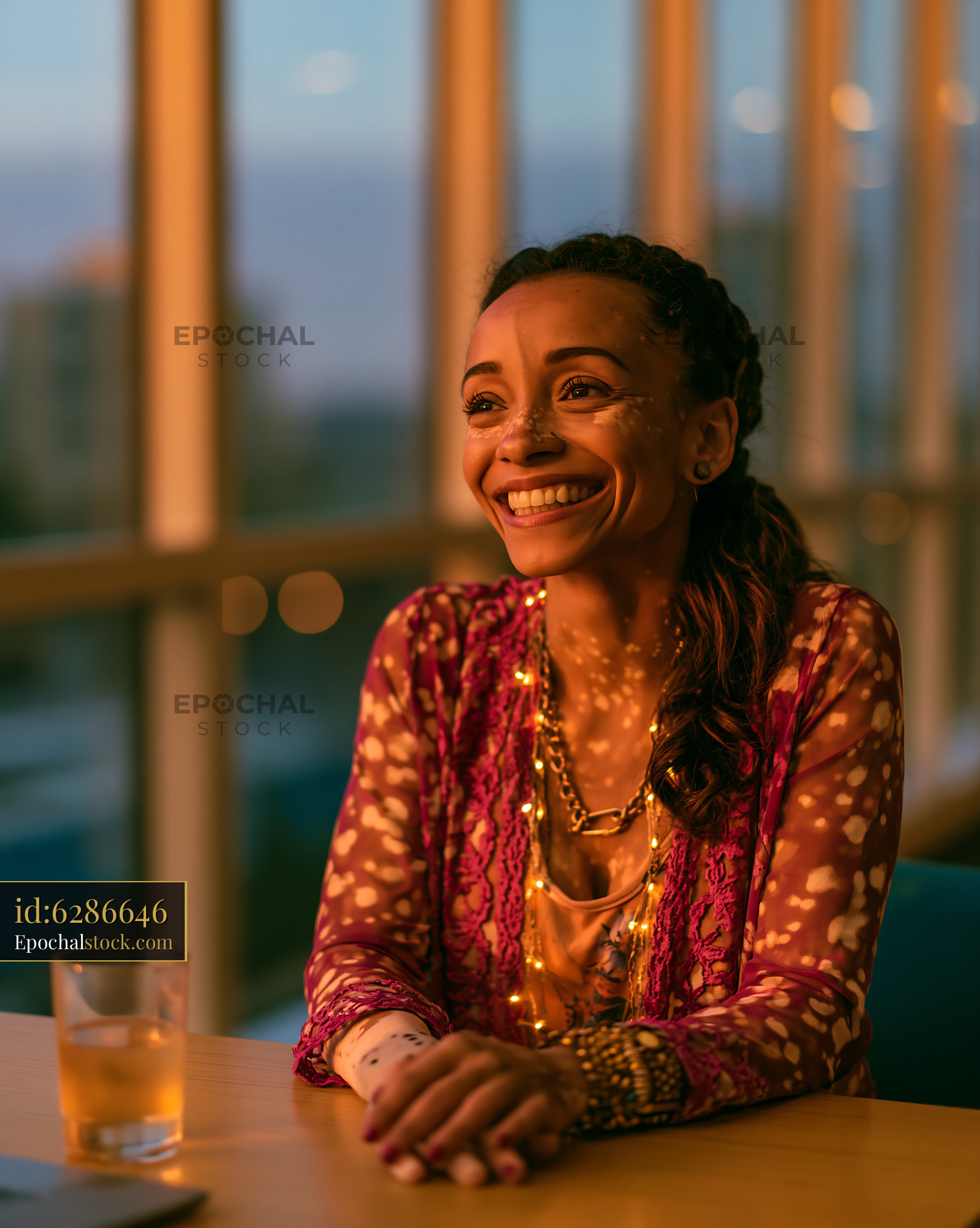 Watermarked full-resolution preview of Woman smiling at sunset while sitting at a table in a bright room
