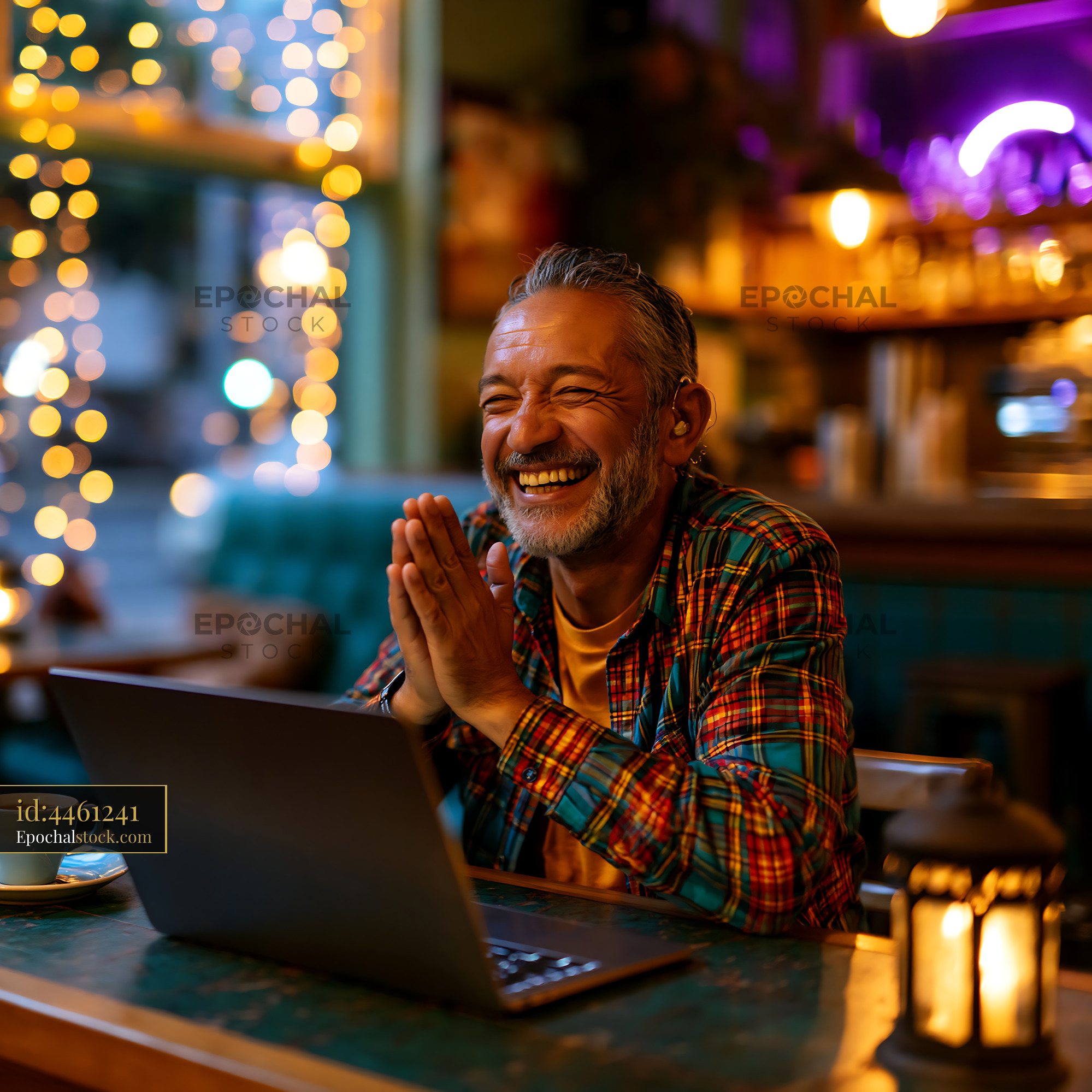 Watermarked full-resolution preview of Man smiling while working on laptop in cafe with warm lighting