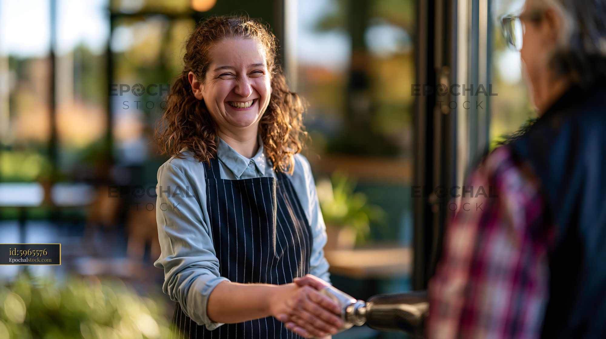 Watermarked full-resolution preview of Employee welcomes customer at the entrance of a cafe