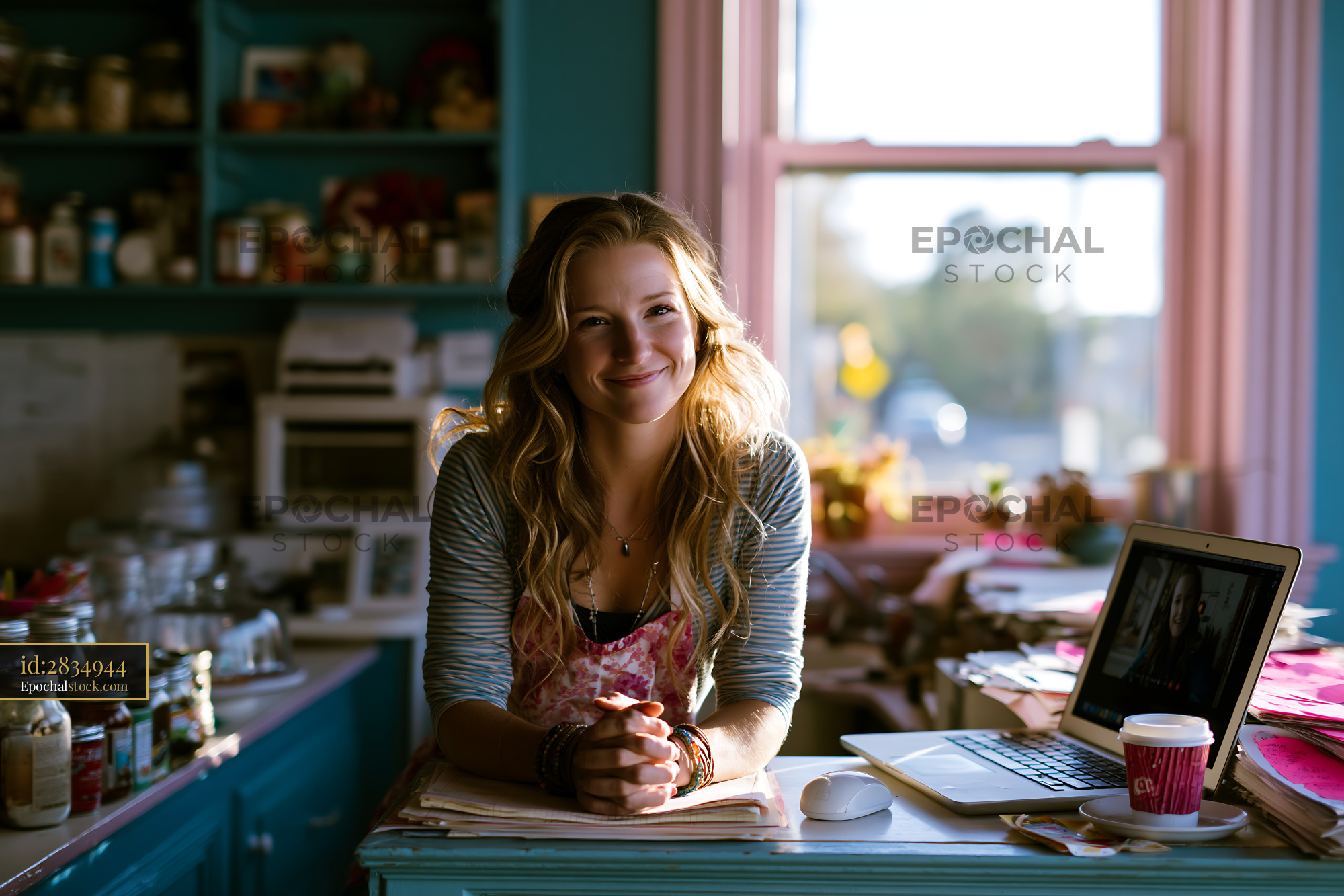 Watermarked full-resolution preview of Young woman smiling in a bright kitchen with a laptop