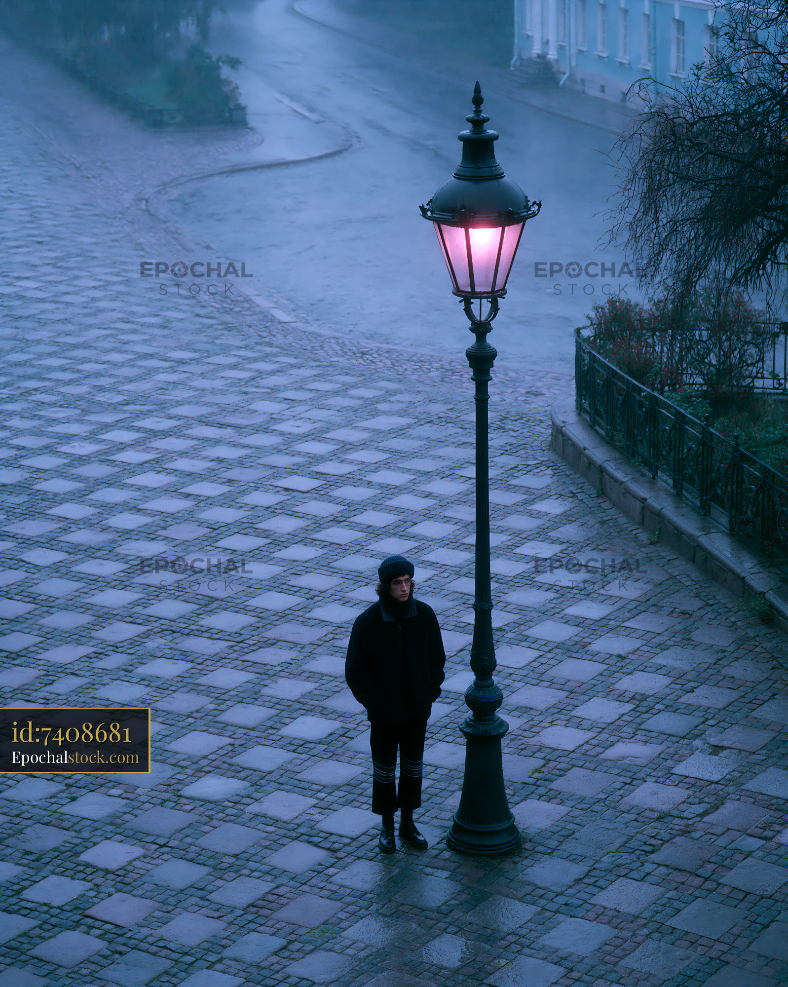 Watermarked full-resolution preview of Person standing under a lamp post on a rainy street