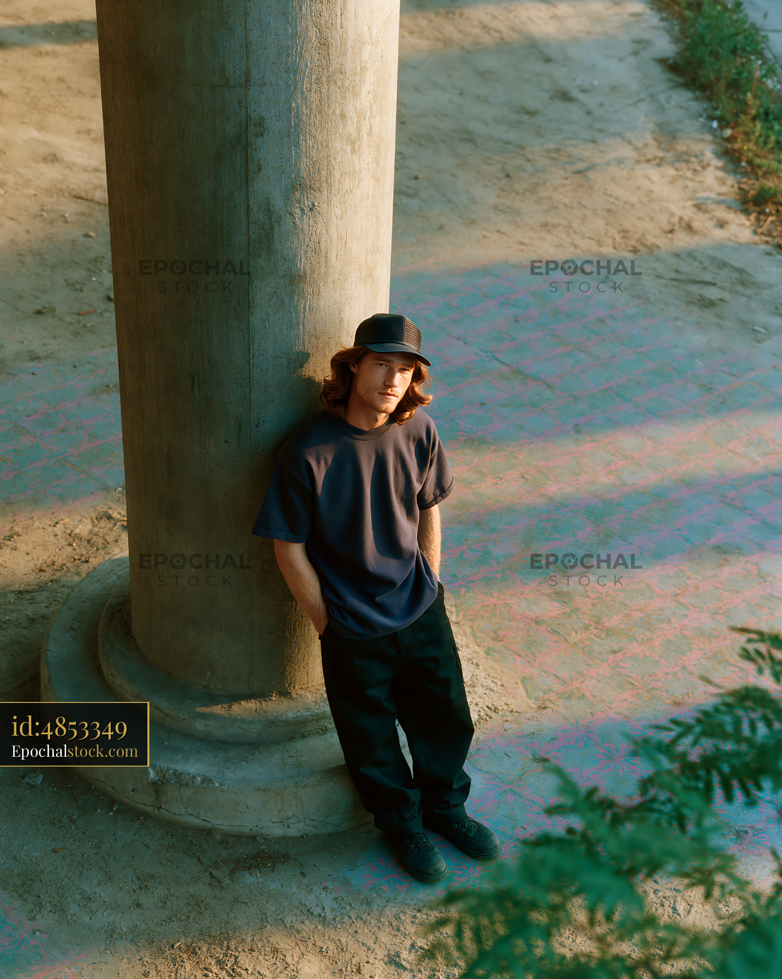 Watermarked full-resolution preview of Young man leaning against a stone pillar on a sunny day