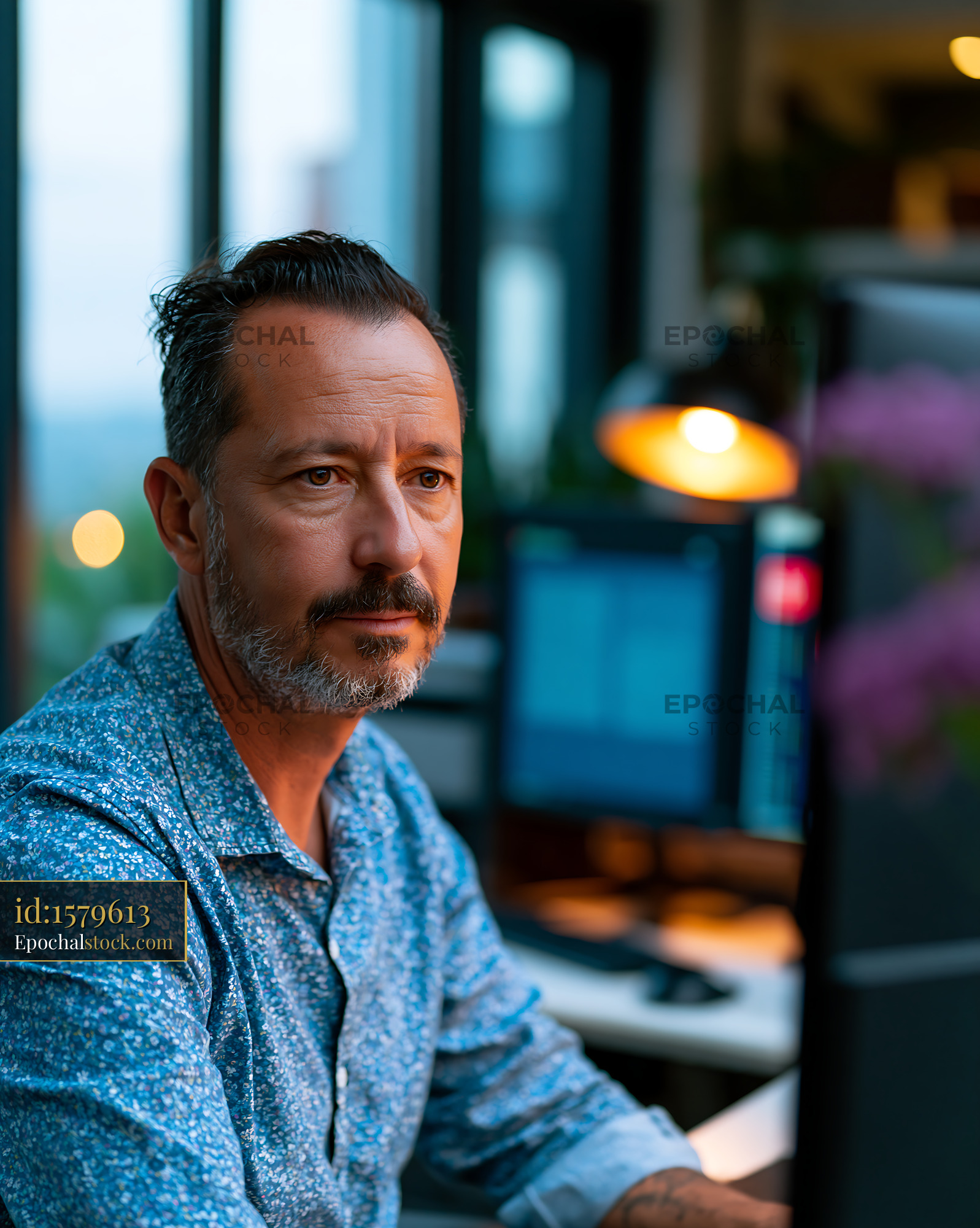 Watermarked full-resolution preview of Man working at a desk with computers in a modern office setting