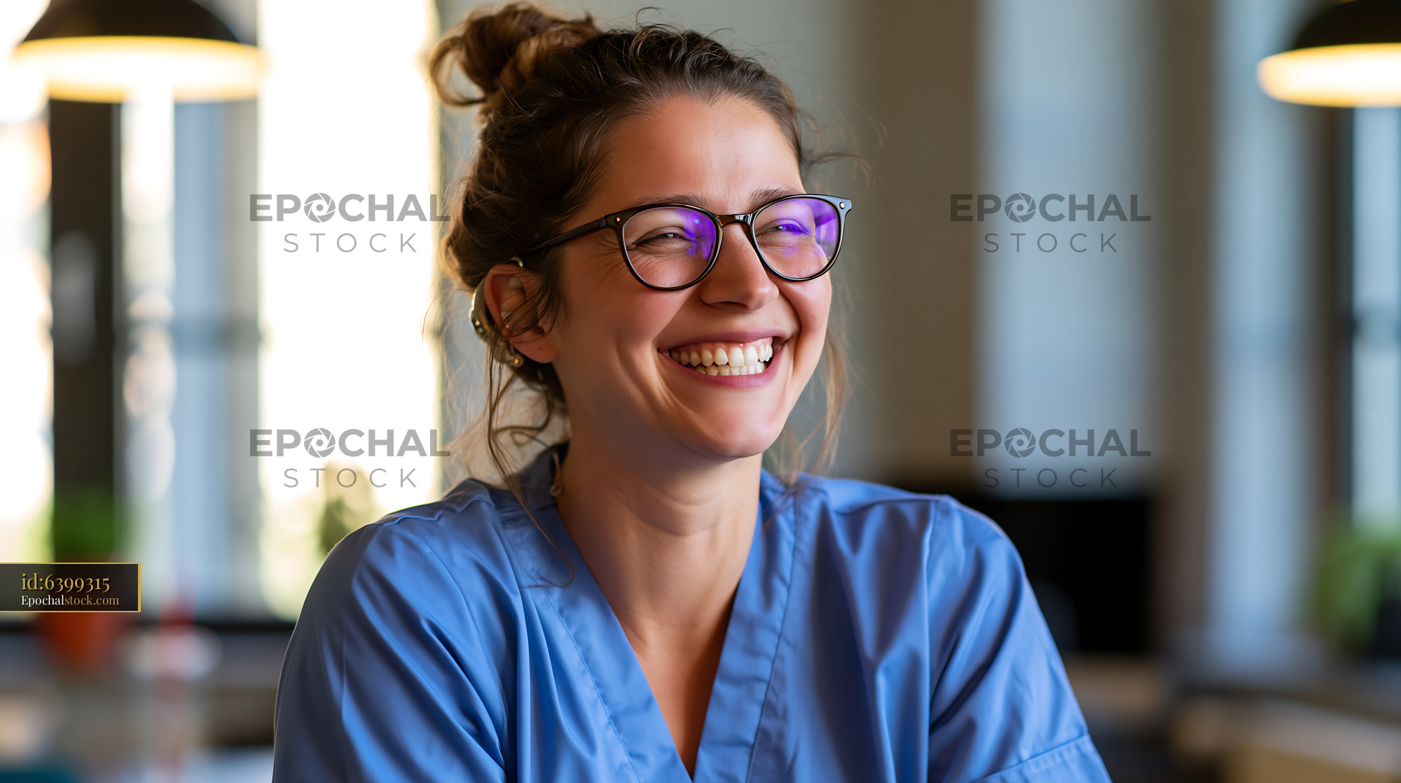 Watermarked full-resolution preview of Smiling nurse in blue scrubs at a bright indoor setting
