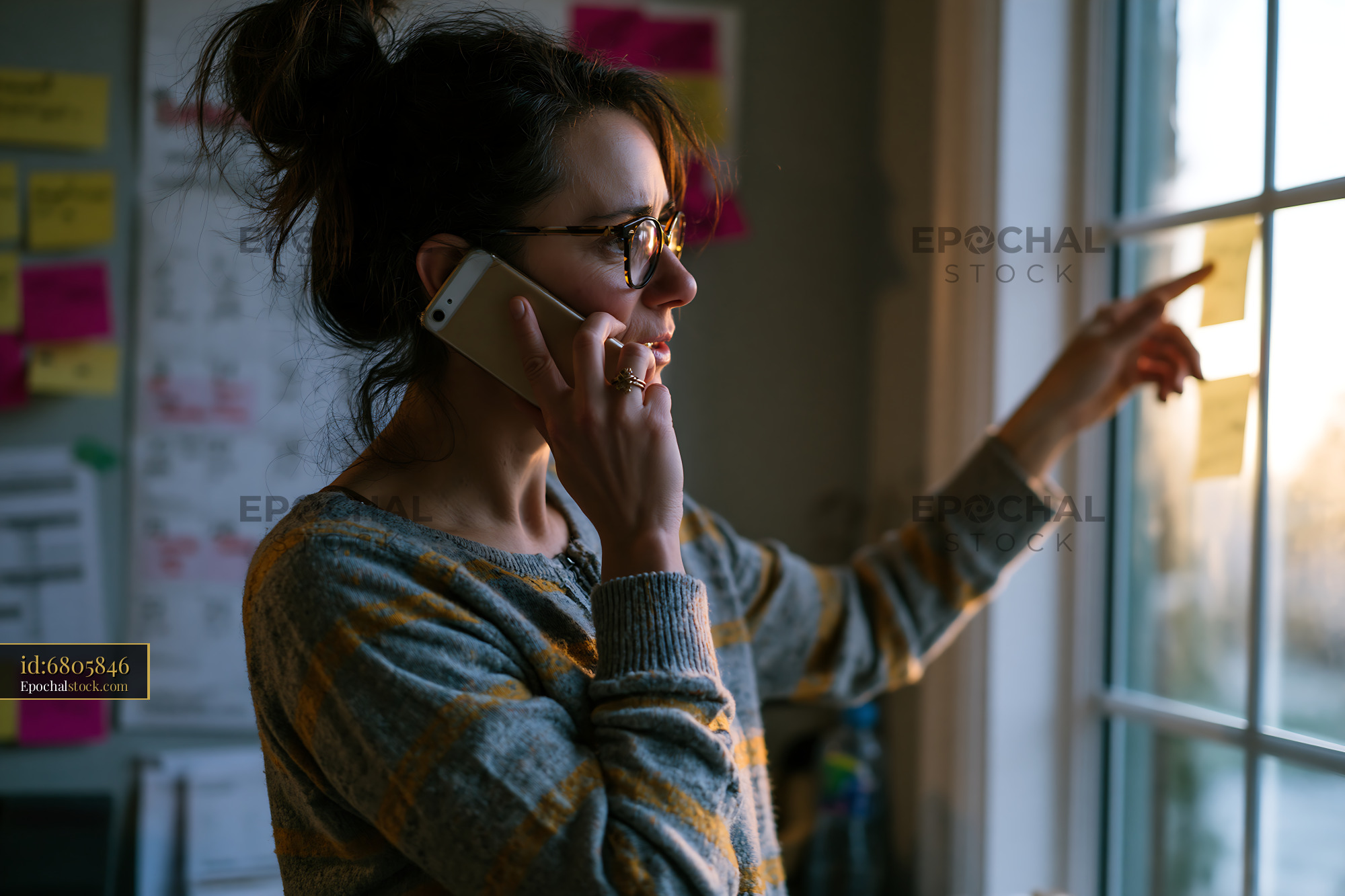 Watermarked full-resolution preview of Woman on phone pointing at window with sticky notes in background