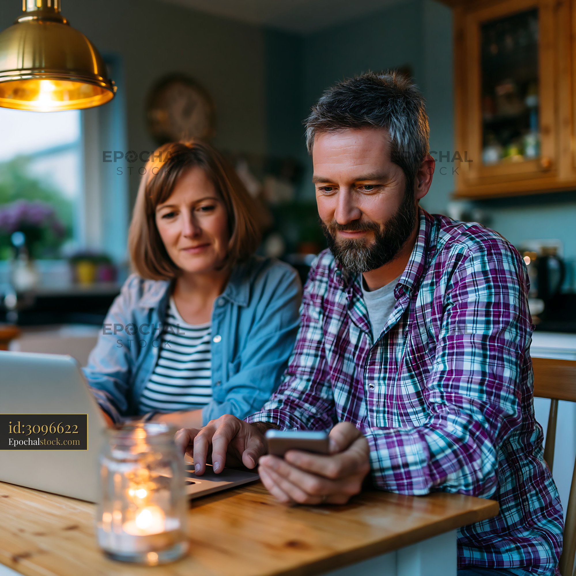 Watermarked full-resolution preview of Couple using laptop and smartphone at home in evening