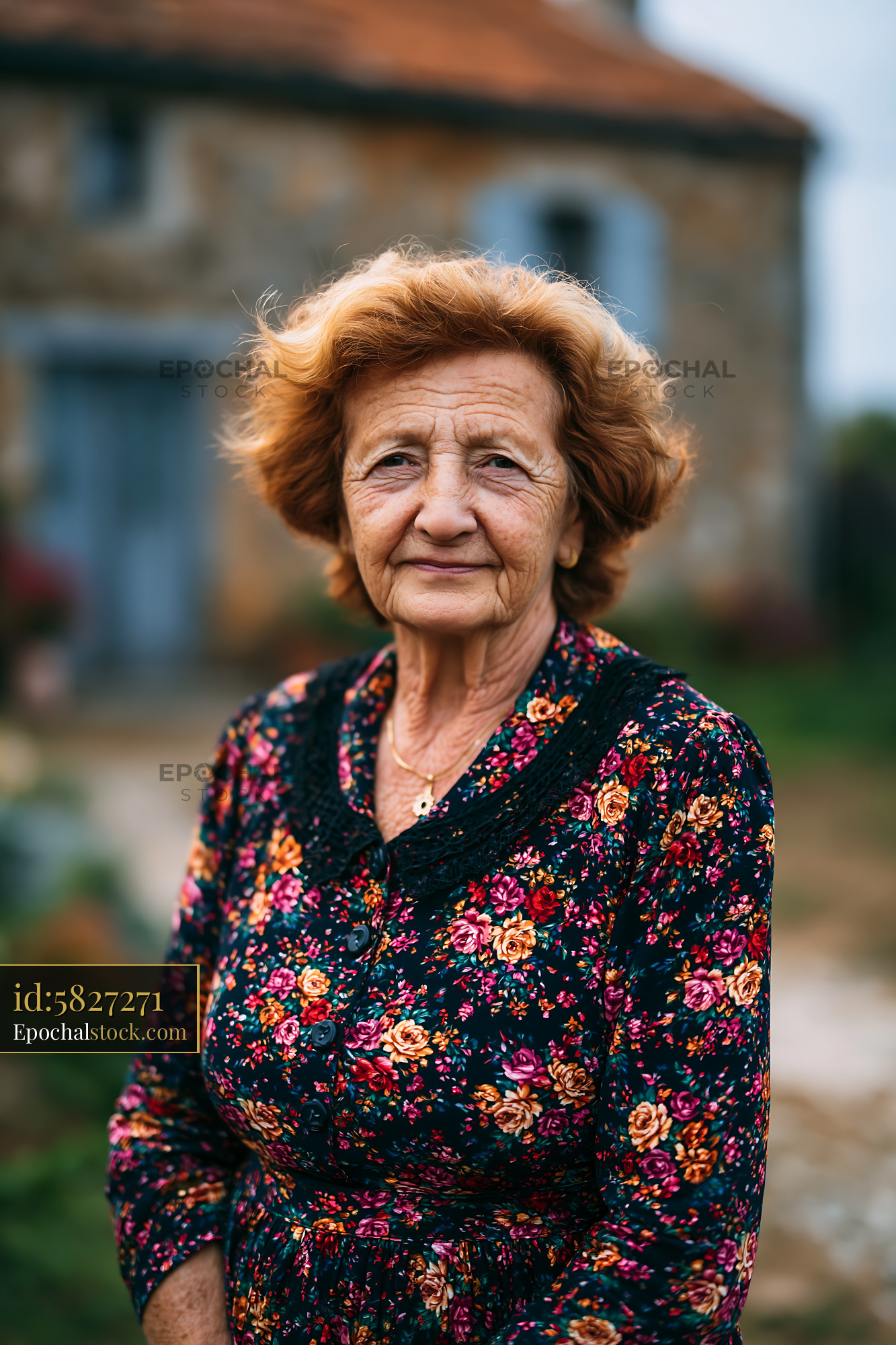 Watermarked full-resolution preview of Elderly woman standing outdoors near a rustic stone house