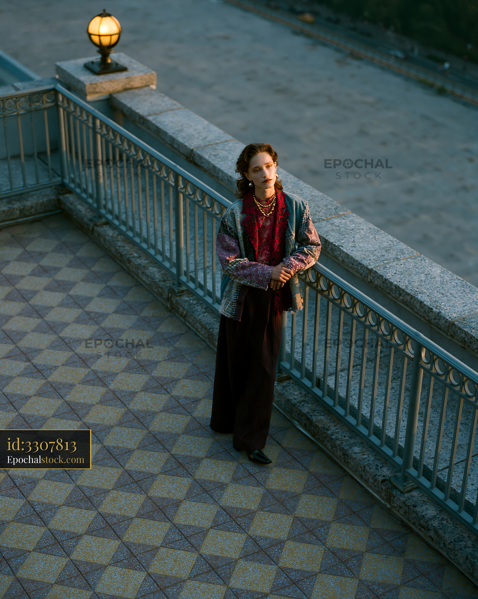 Watermarked full-resolution preview of Woman standing on a balcony overlooking a city street at sunset
