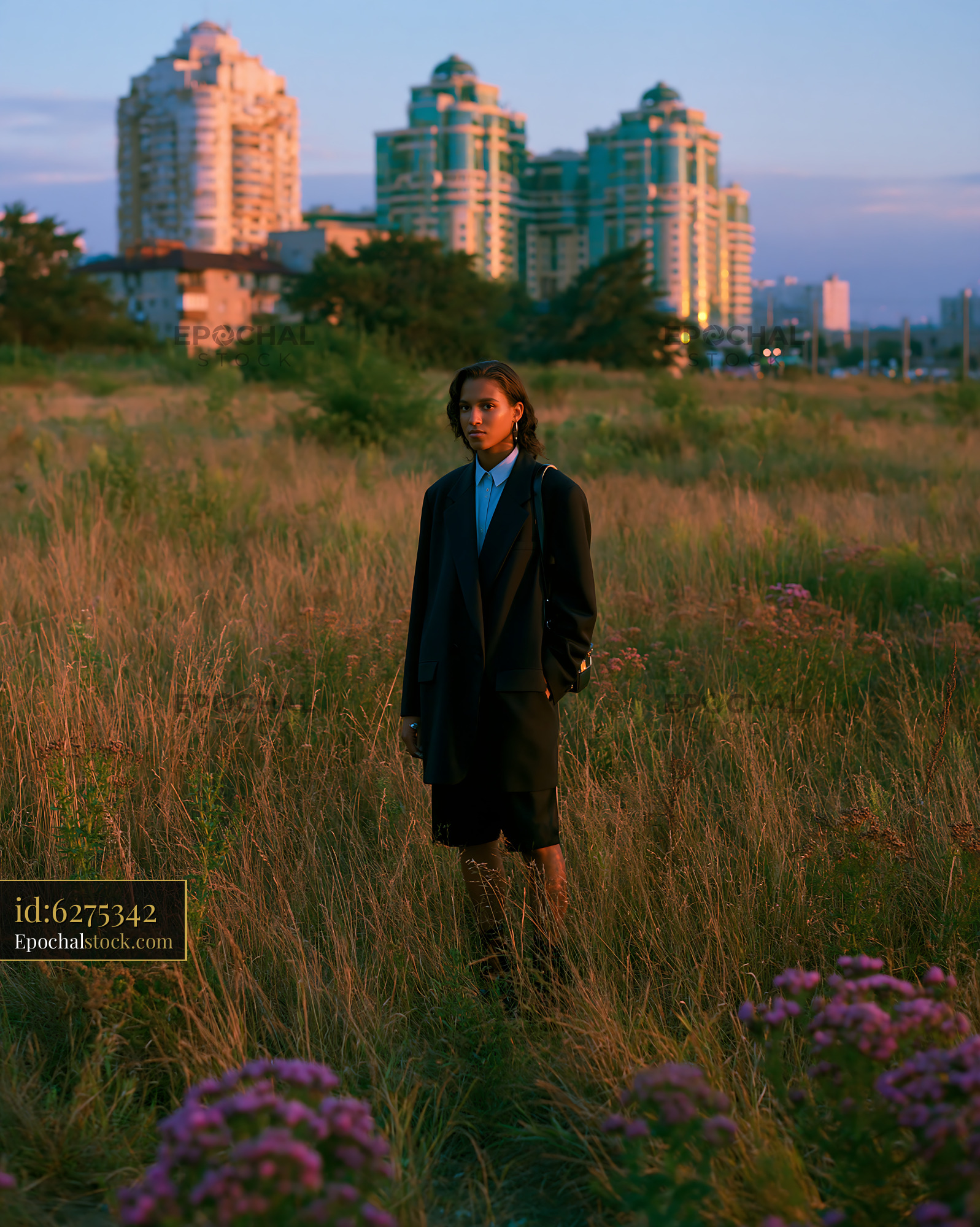 Woman in Oversized Blazer and Bike Shorts Standing in Field at Sunset - stock photo