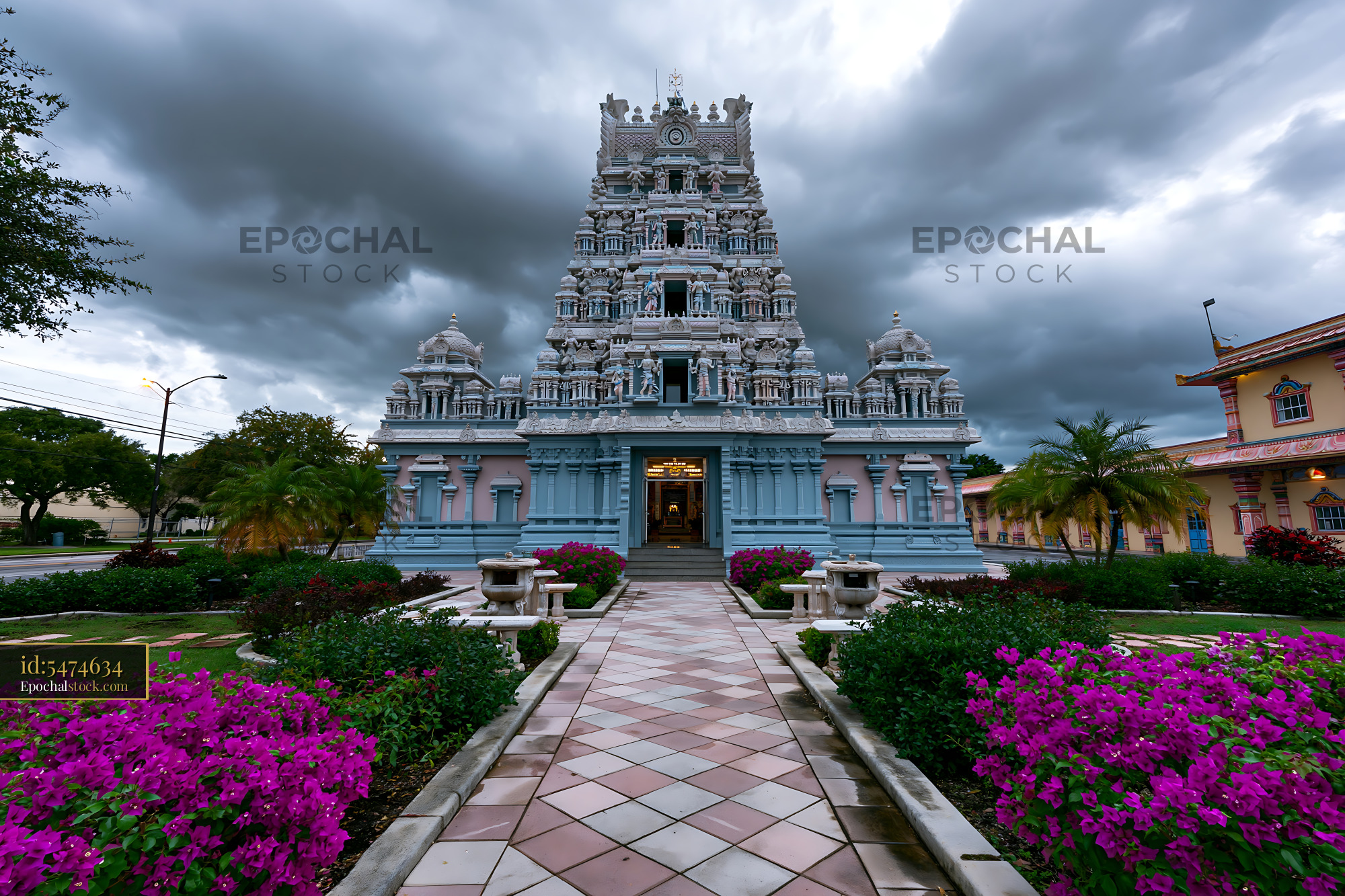 Watermarked full-resolution preview of Ornate Hindu temple with flower-lined walkway and stormy sky