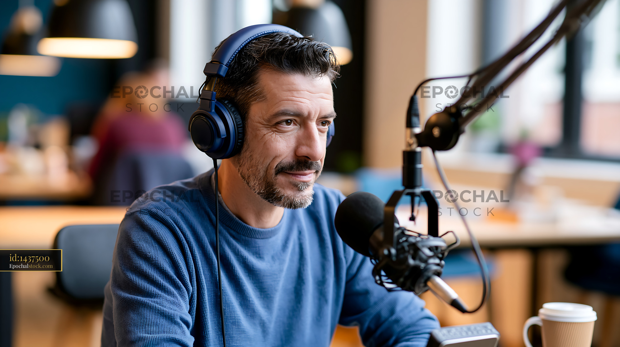 Watermarked full-resolution preview of Man wearing headphones speaking into a microphone in a workspace