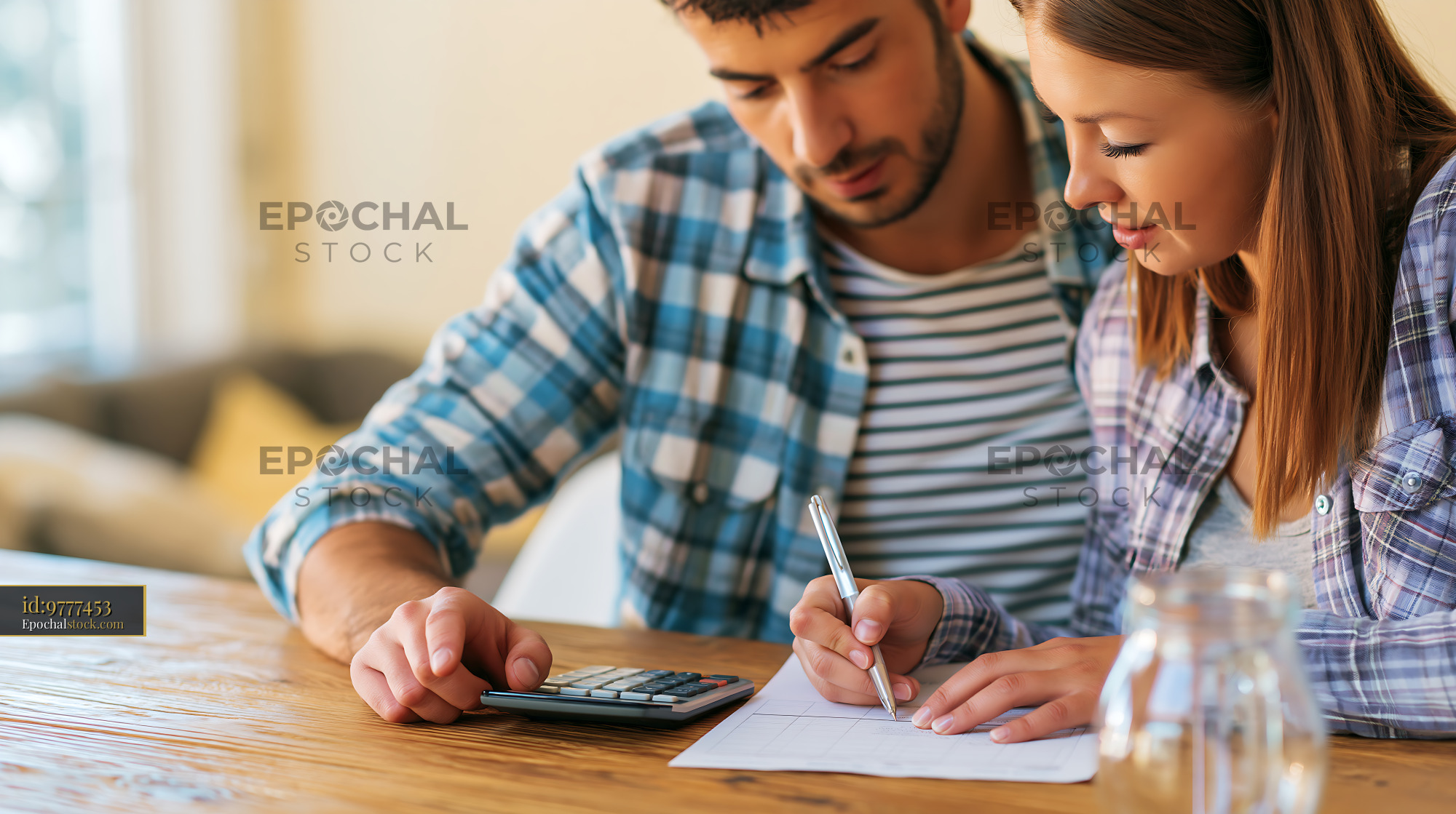 Watermarked full-resolution preview of Couple working on finances at home with calculator and notebook