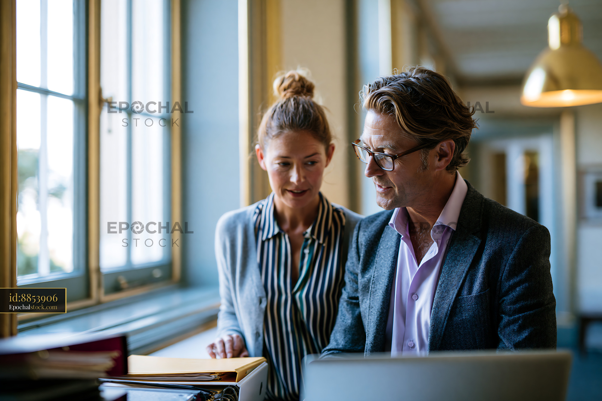 Watermarked full-resolution preview of Two professionals discuss work in a modern office setting