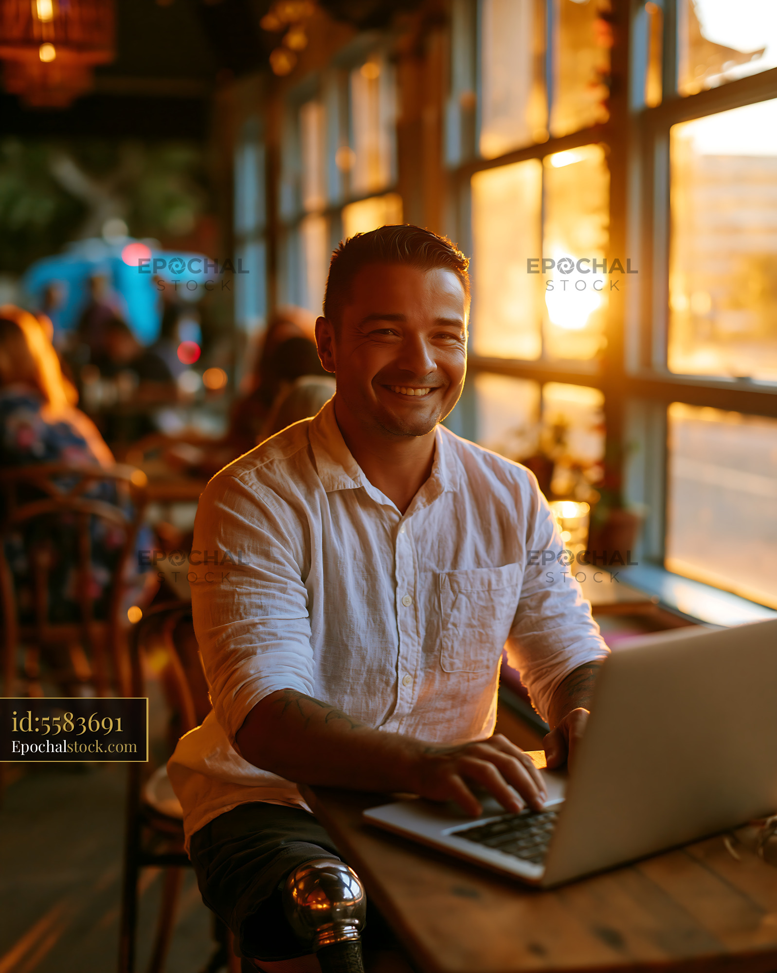 Watermarked full-resolution preview of Smiling man working on a laptop beside cafe windows
