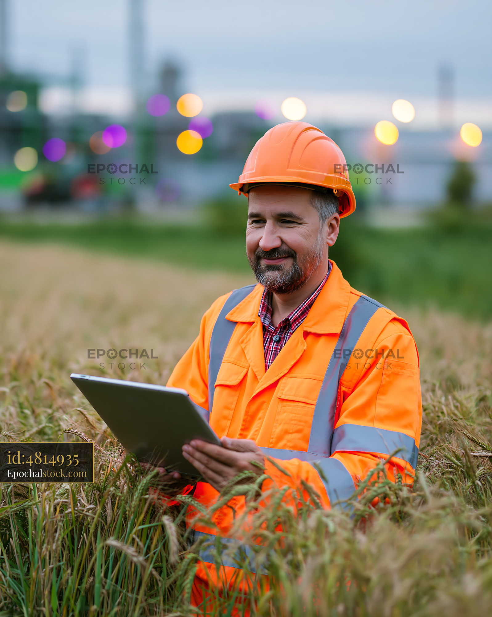 Watermarked full-resolution preview of Worker in orange safety jacket using tablet in wheat field