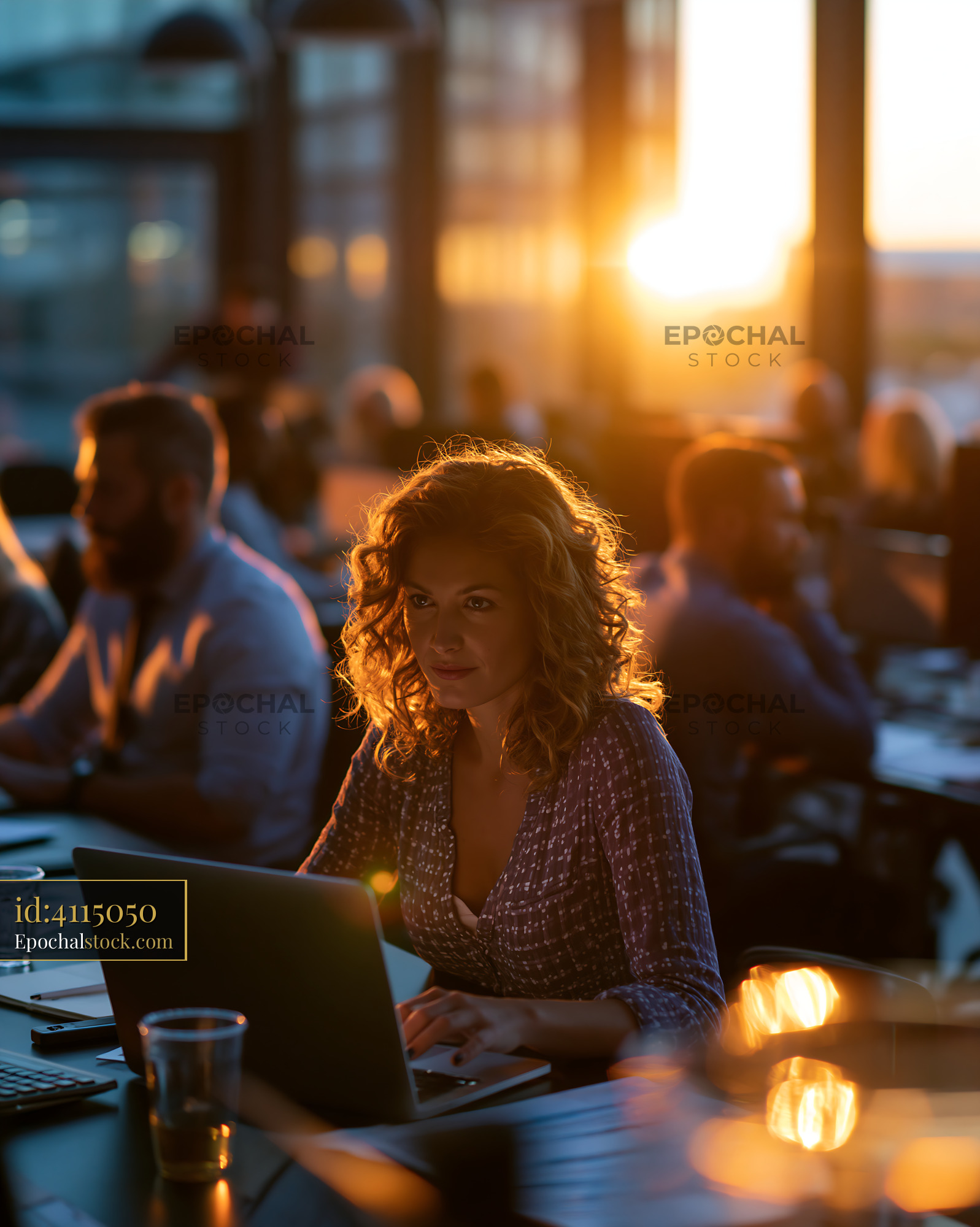 Watermarked full-resolution preview of Woman working on laptop in a busy cafe during sunset