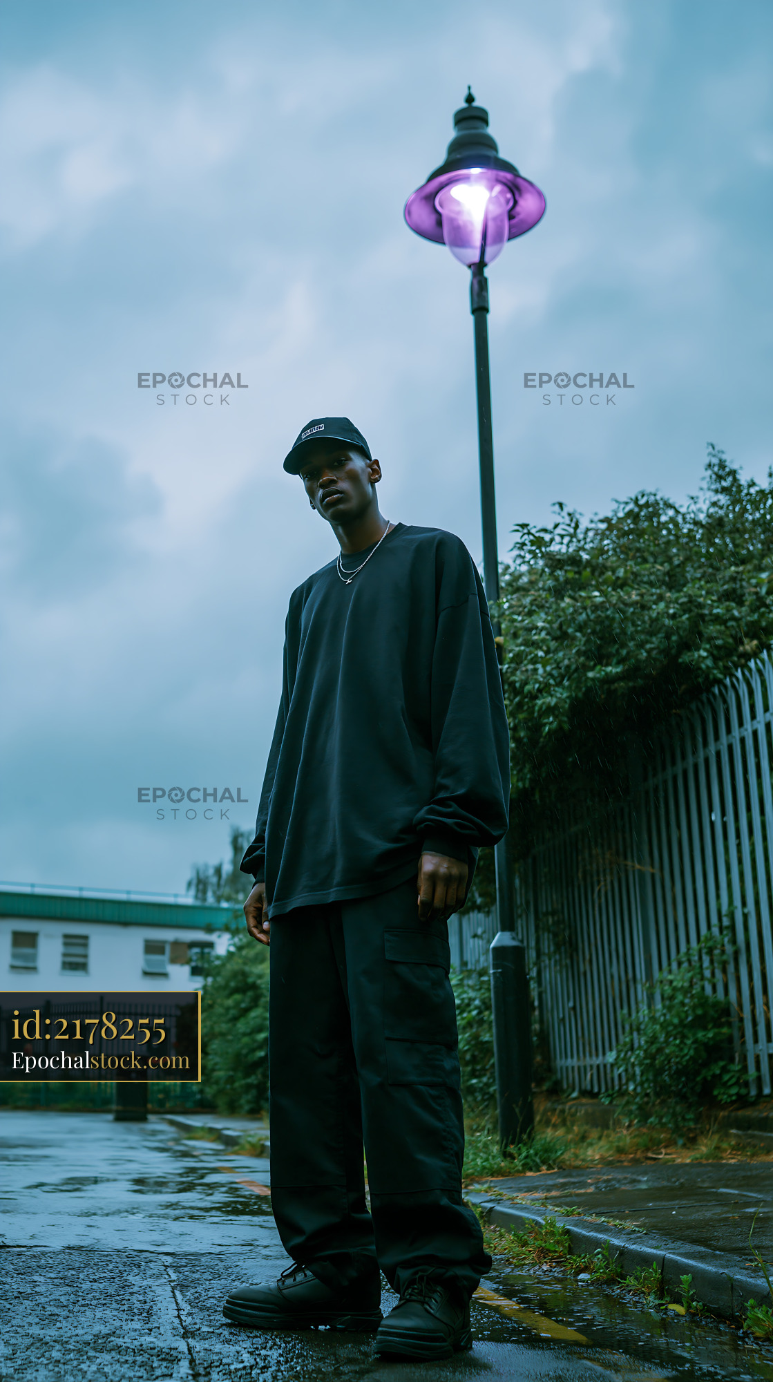 Watermarked full-resolution preview of Man stands under street lamp in urban area on cloudy day