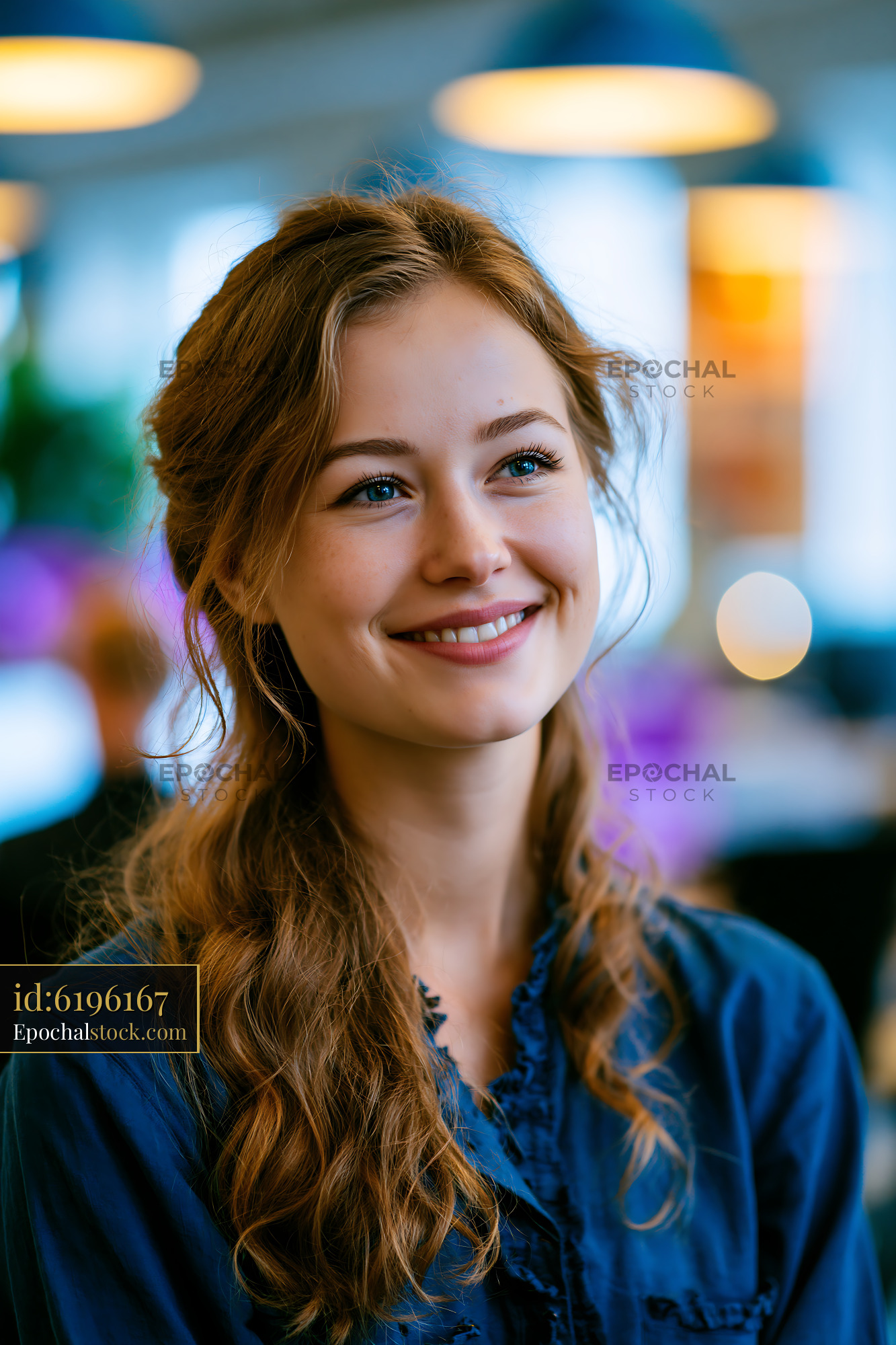 Watermarked full-resolution preview of Smiling woman in blue shirt at a modern workspace