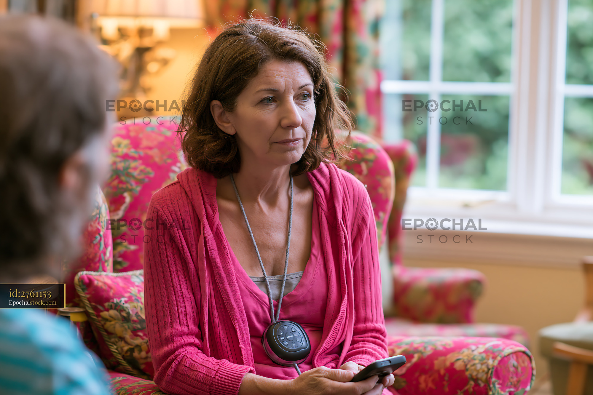 Watermarked full-resolution preview of Woman sitting on a floral couch holding a phone in a cozy room