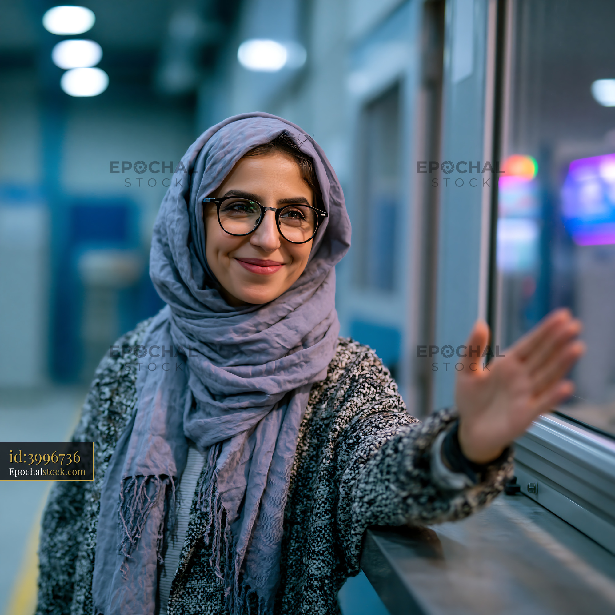 Watermarked full-resolution preview of Woman in a gray scarf smiling and waving indoors
