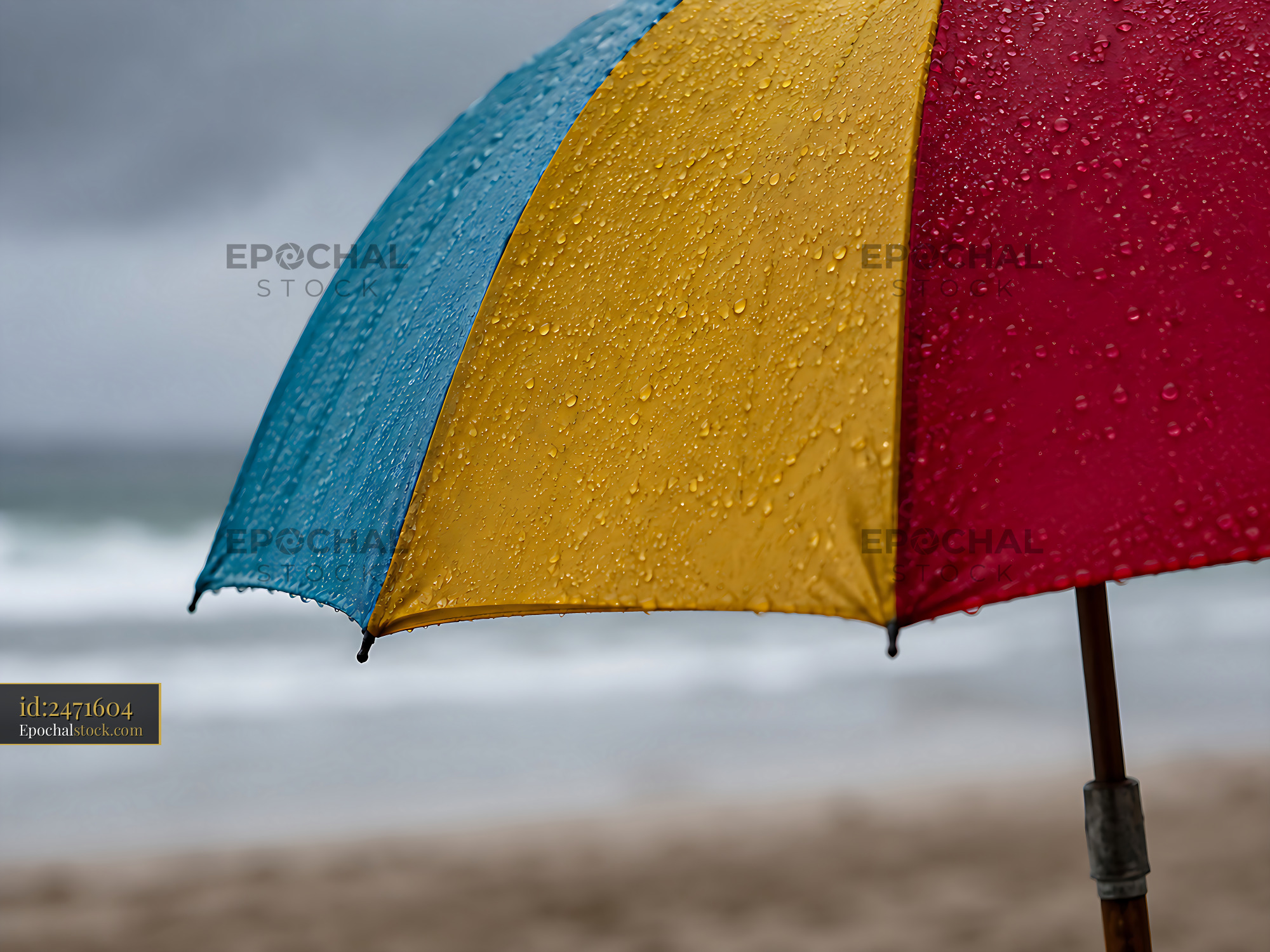 Watermarked full-resolution preview of Bright umbrella on a rainy beach with ocean waves in the background