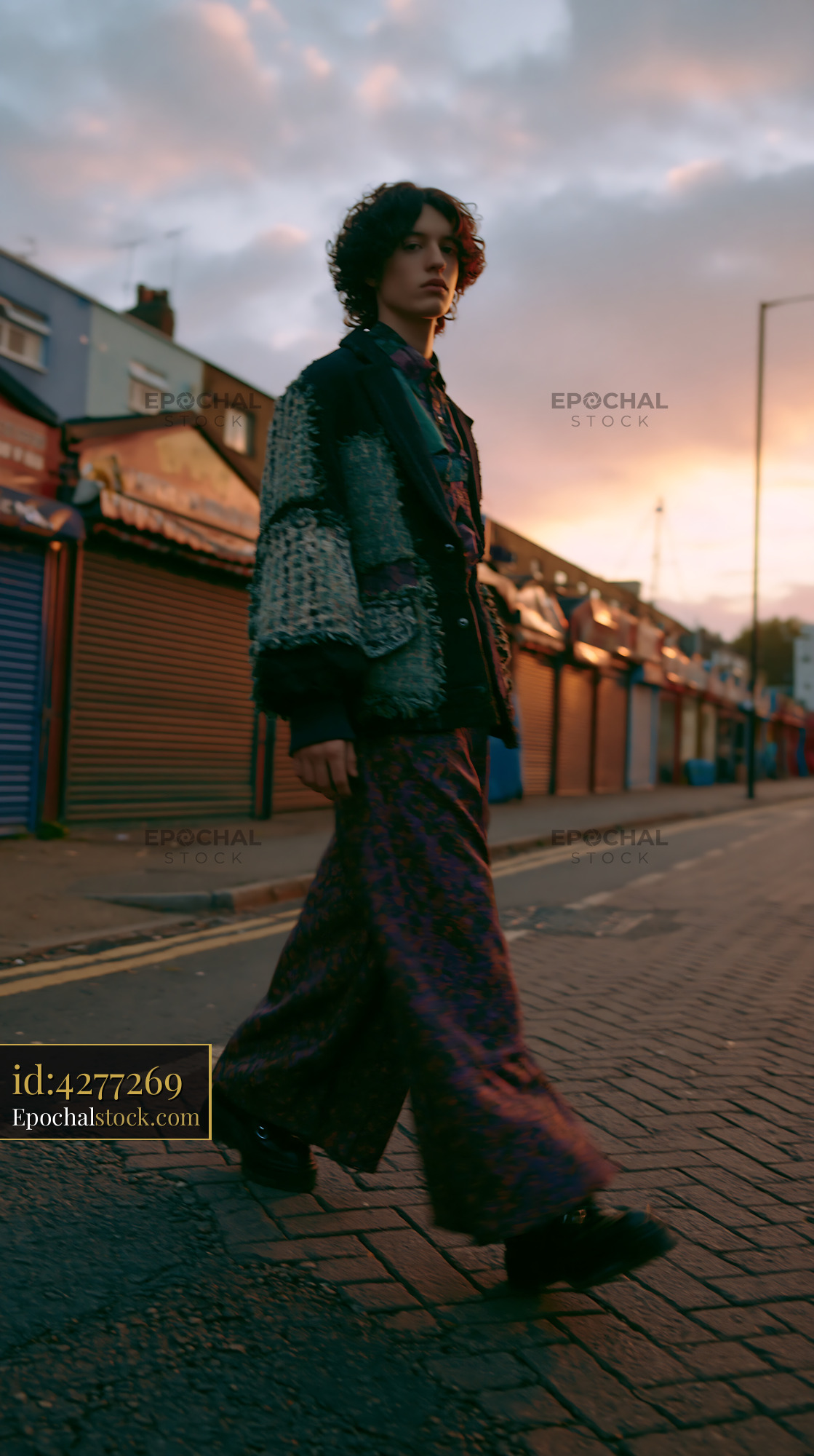 Watermarked full-resolution preview of Person walking on a city street at sunset with closed shops nearby