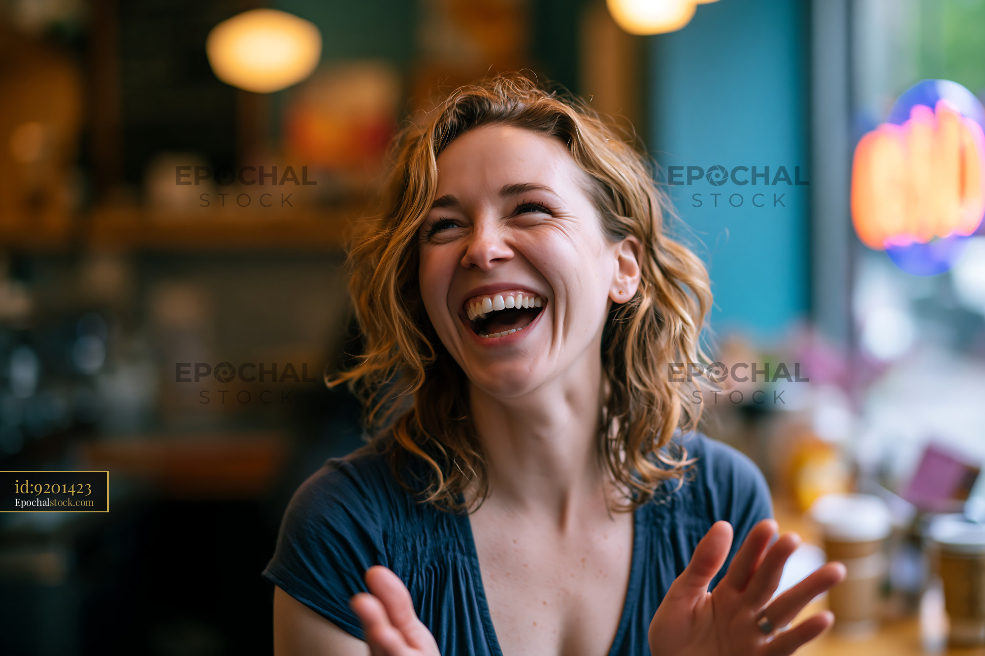 Watermarked full-resolution preview of Woman laughing in a cafe with bright lights and blurred background