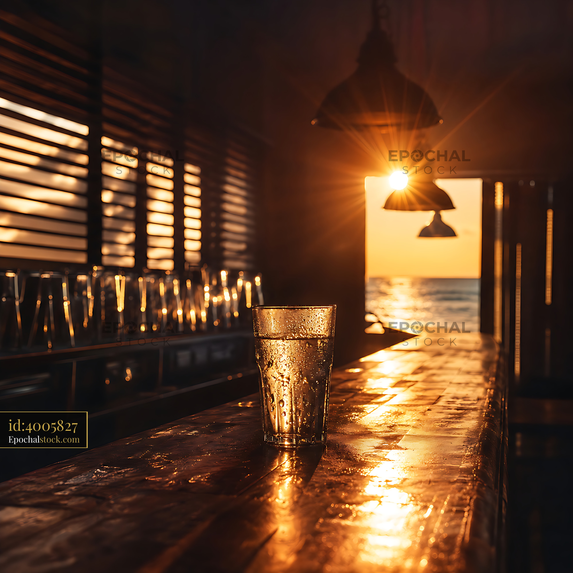 Glass of Water Sits on a Wooden Bar at Sunset Near the Ocean - stock photo