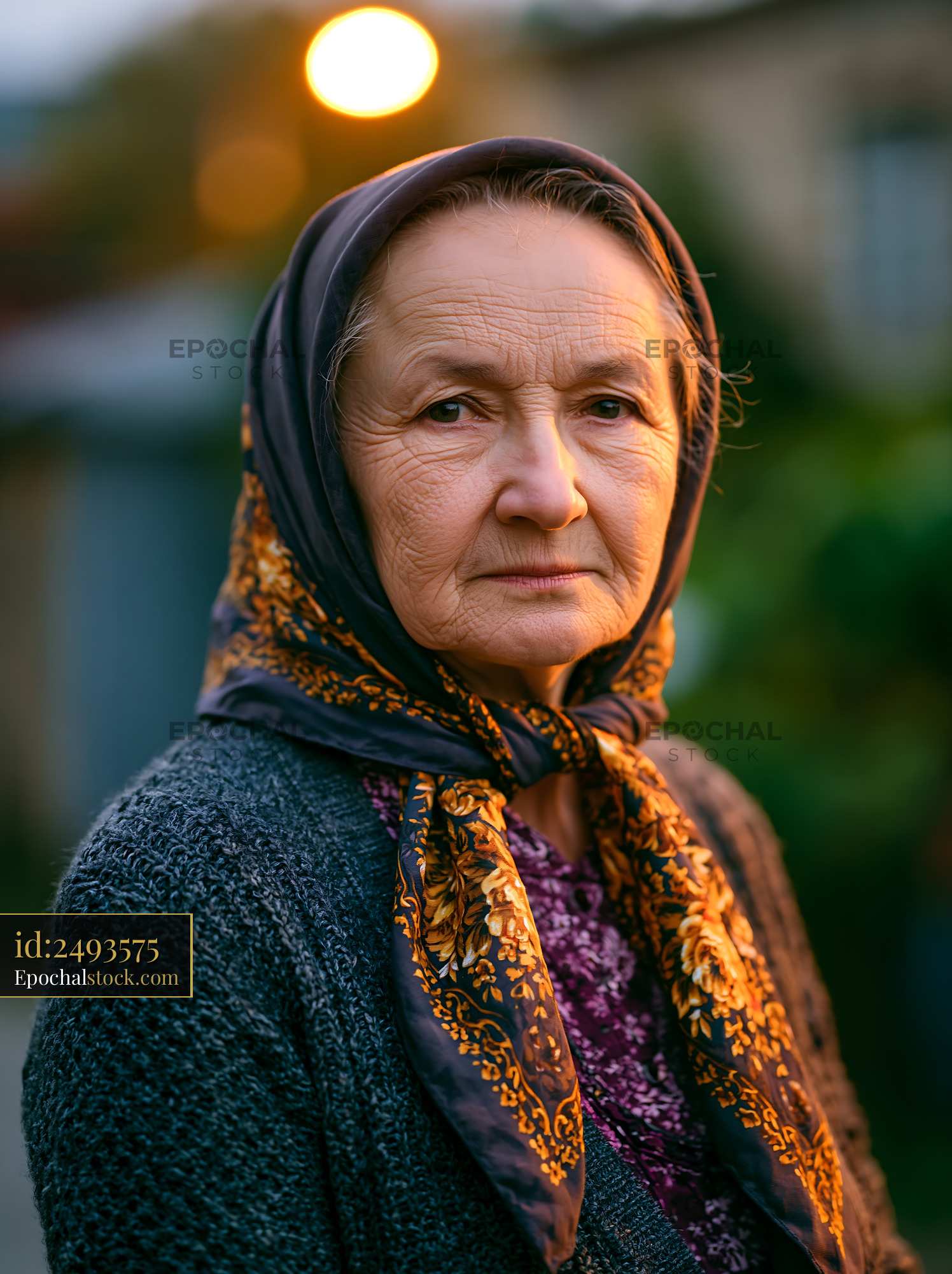Watermarked full-resolution preview of Elderly woman in a headscarf standing outdoors during twilight
