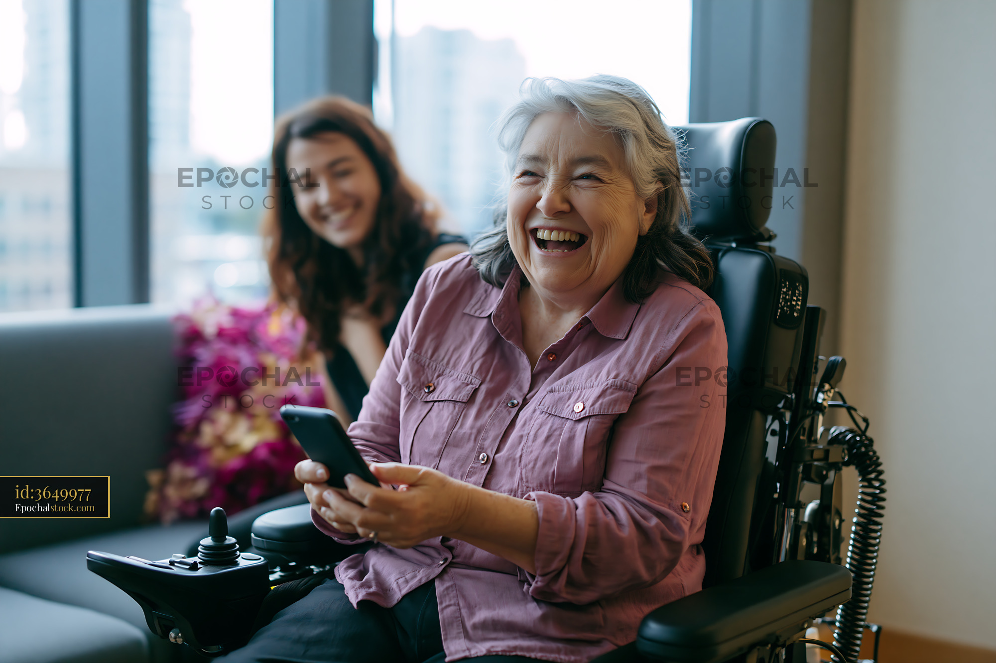 Watermarked full-resolution preview of Smiling woman in wheelchair using phone with friend nearby