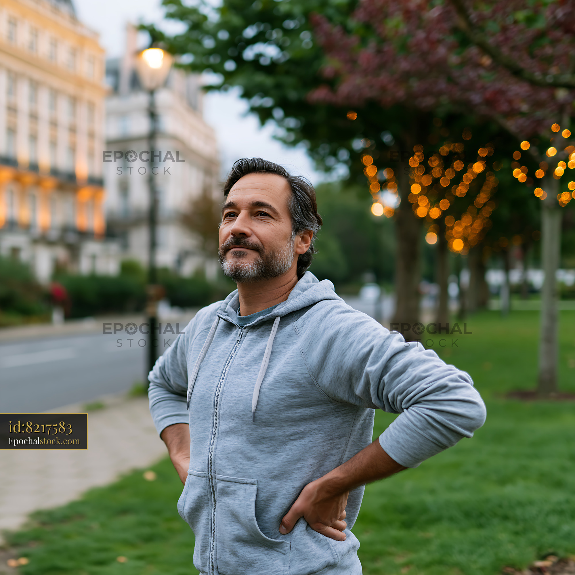 Watermarked full-resolution preview of Man standing in a park with hands on hips during twilight hours