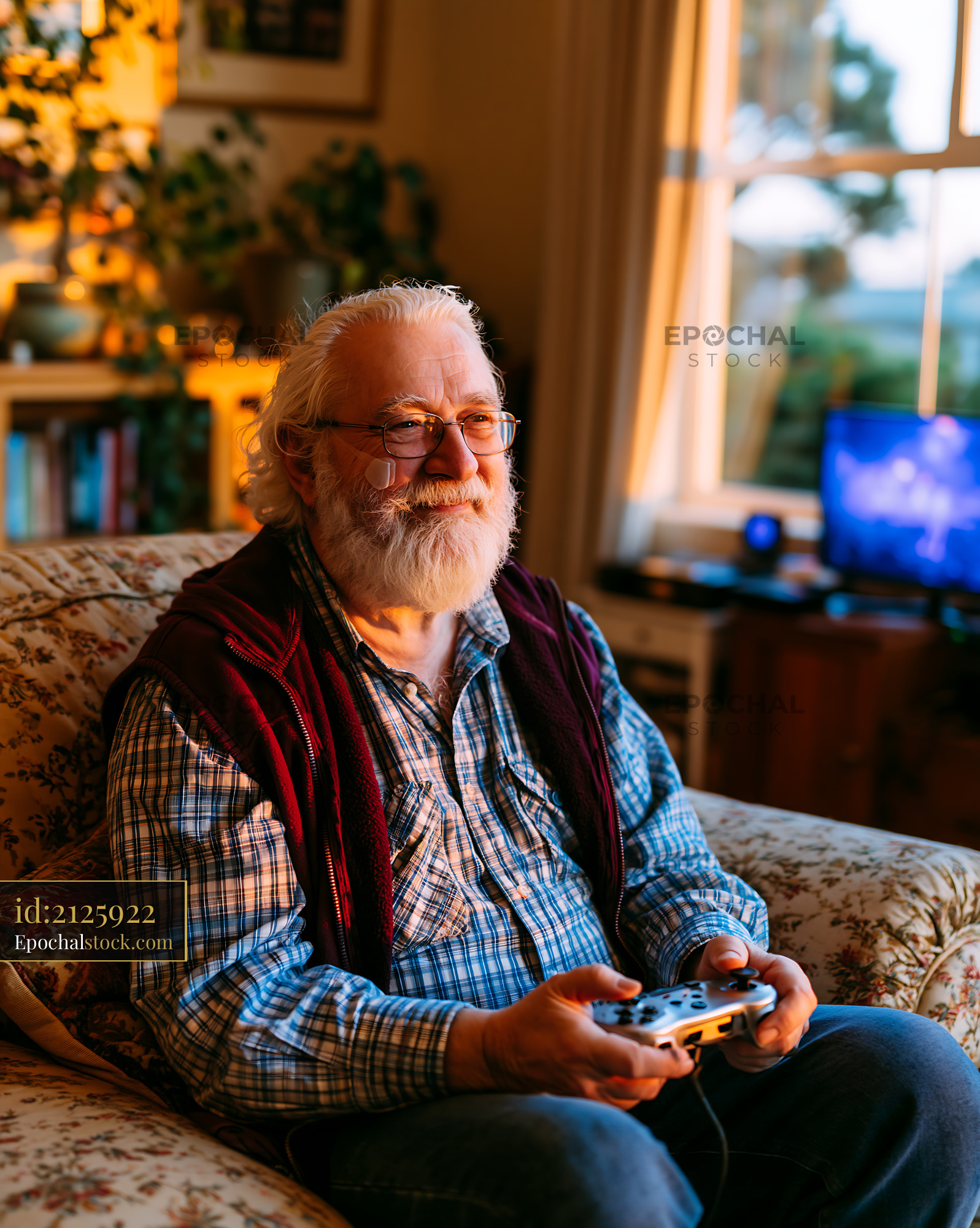 Watermarked full-resolution preview of Senior man playing video games on a cozy sofa in a well-lit room