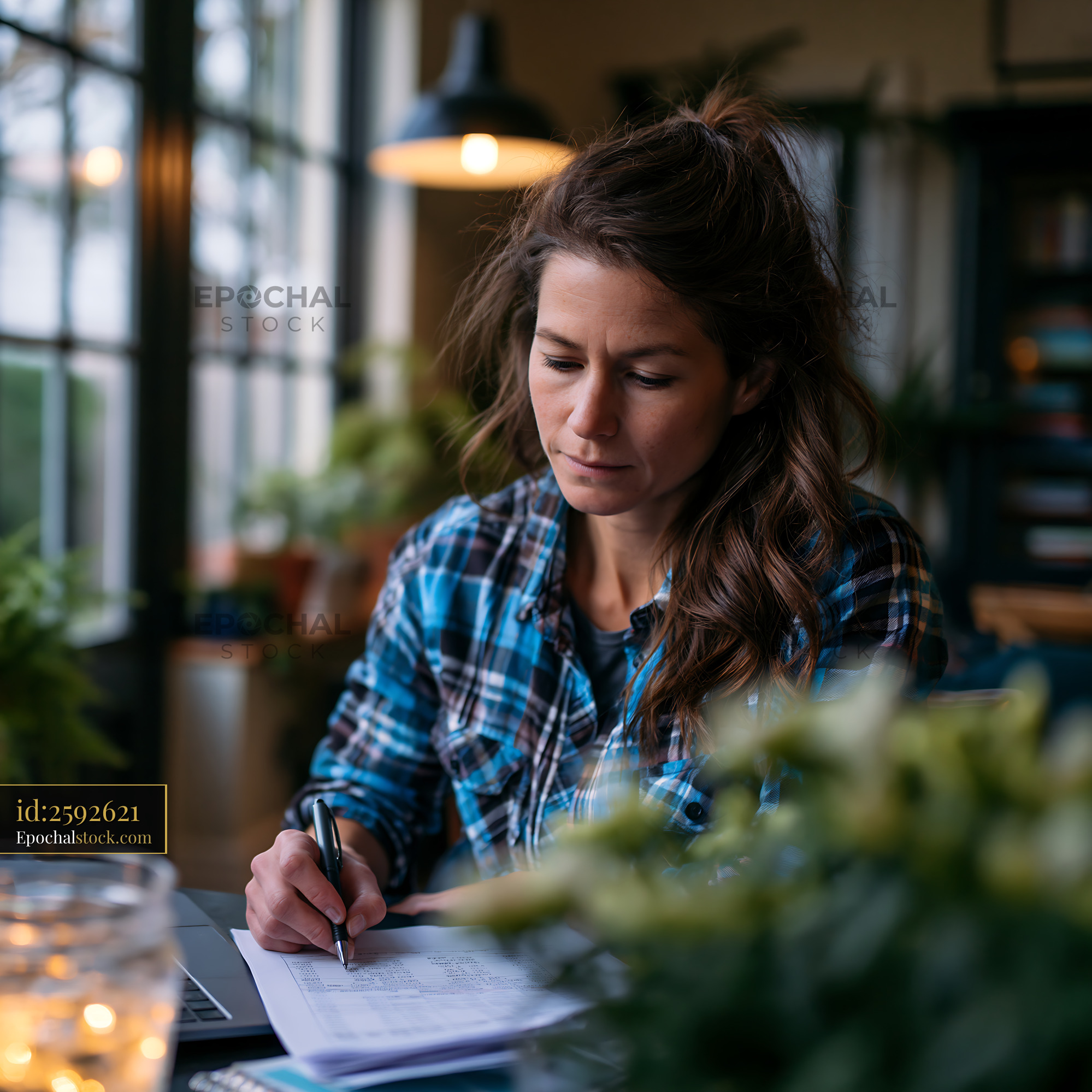 Watermarked full-resolution preview of Woman writing notes at a desk surrounded by plants in a cozy setting