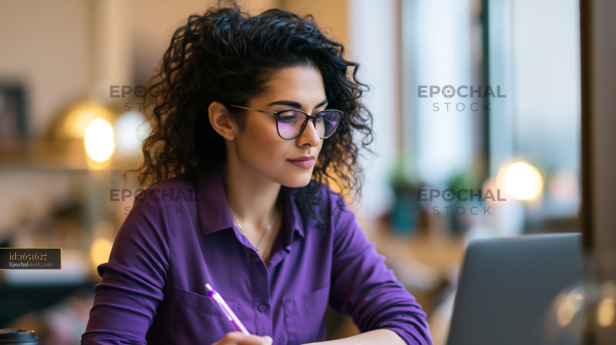 Watermarked full-resolution preview of Woman working at a desk with a laptop and writing notes