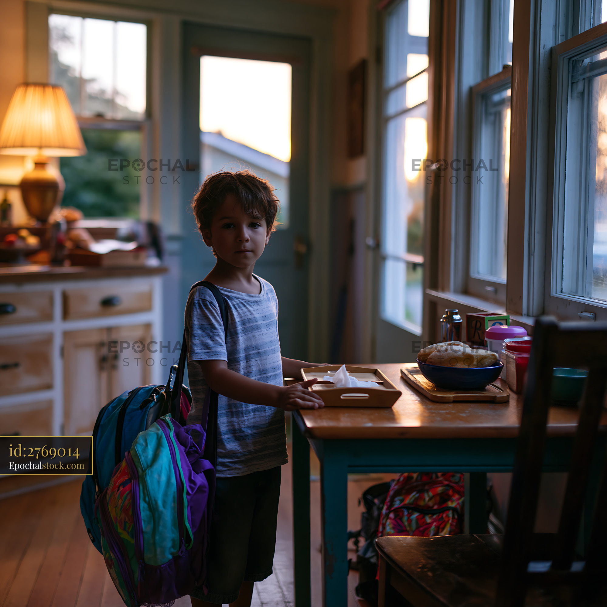 Watermarked full-resolution preview of Child with backpack standing by kitchen table at sunset