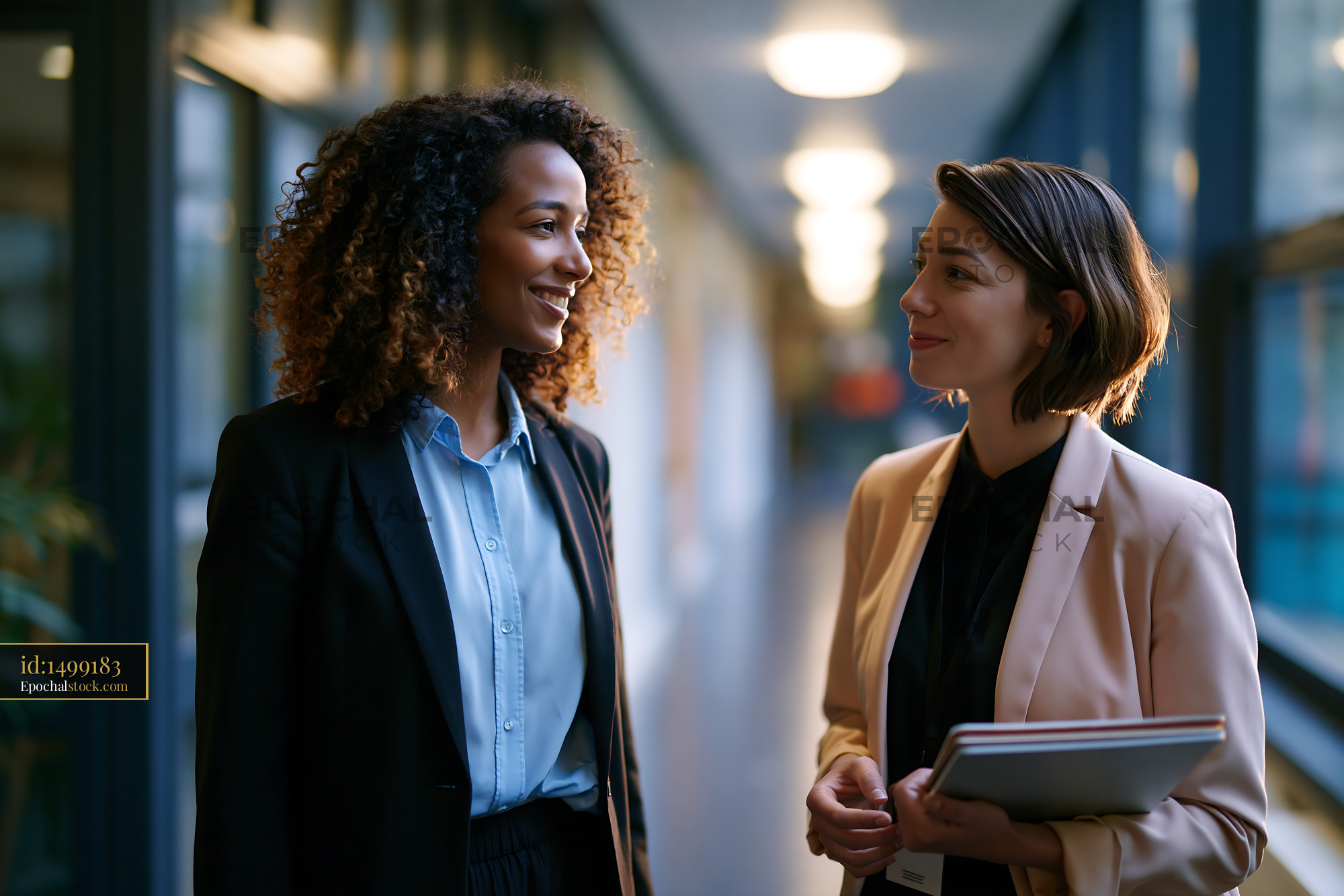 Watermarked full-resolution preview of Two women talking in a modern office corridor during daytime