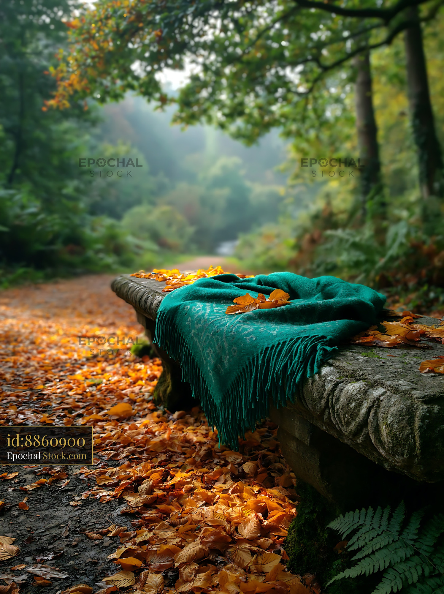 Teal blanket on a stone bench covered in autumn leaves in a misty fore - stock photo