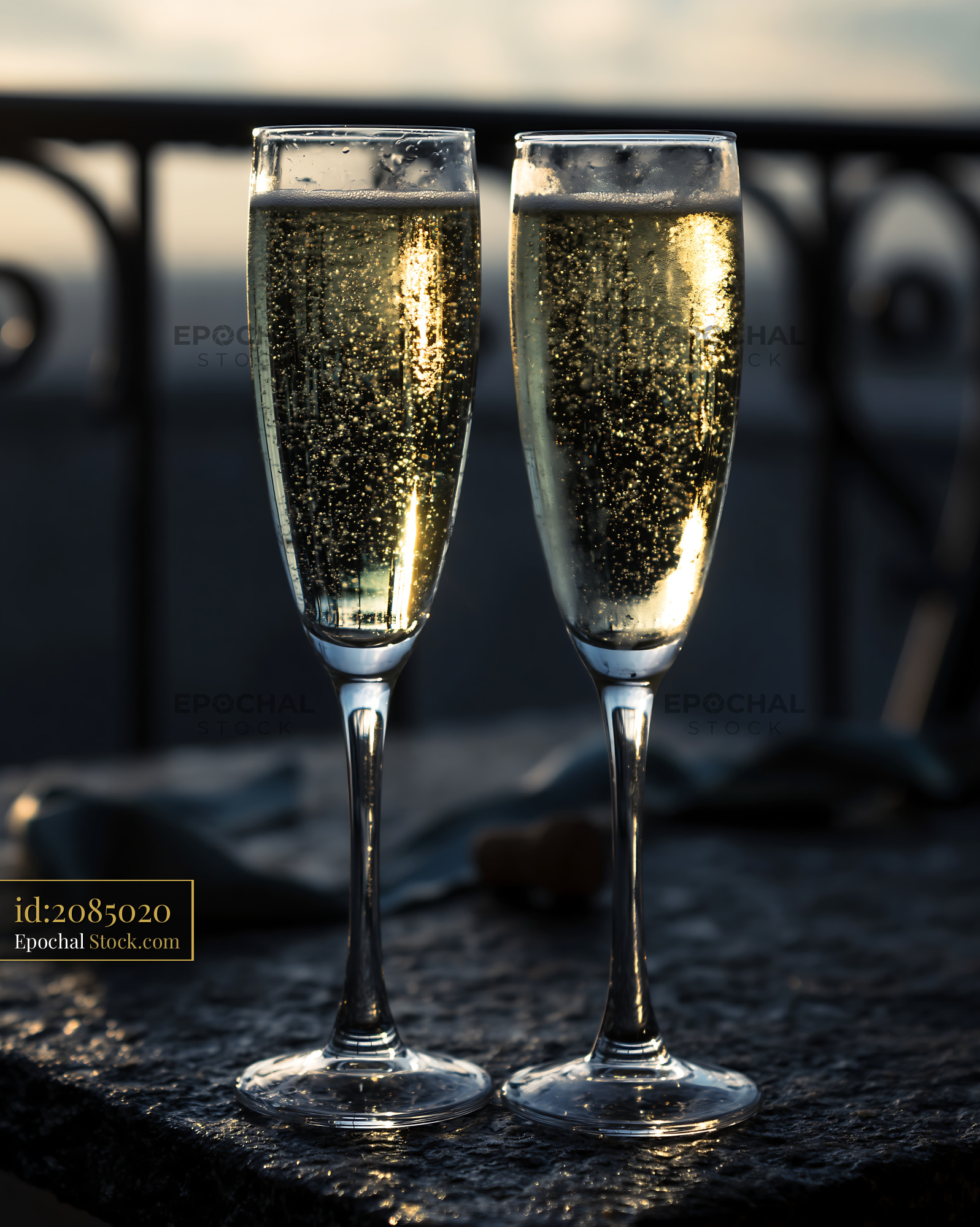 Two champagne flutes with golden bubbles at sunset on a balcony - stock photo