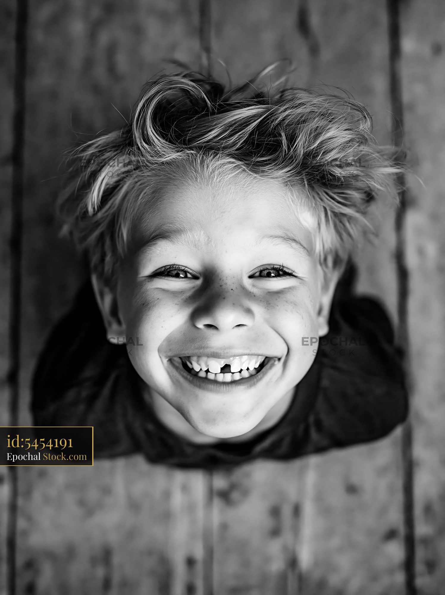 Young boy with messy hair and a missing front tooth smiling up - stock photo