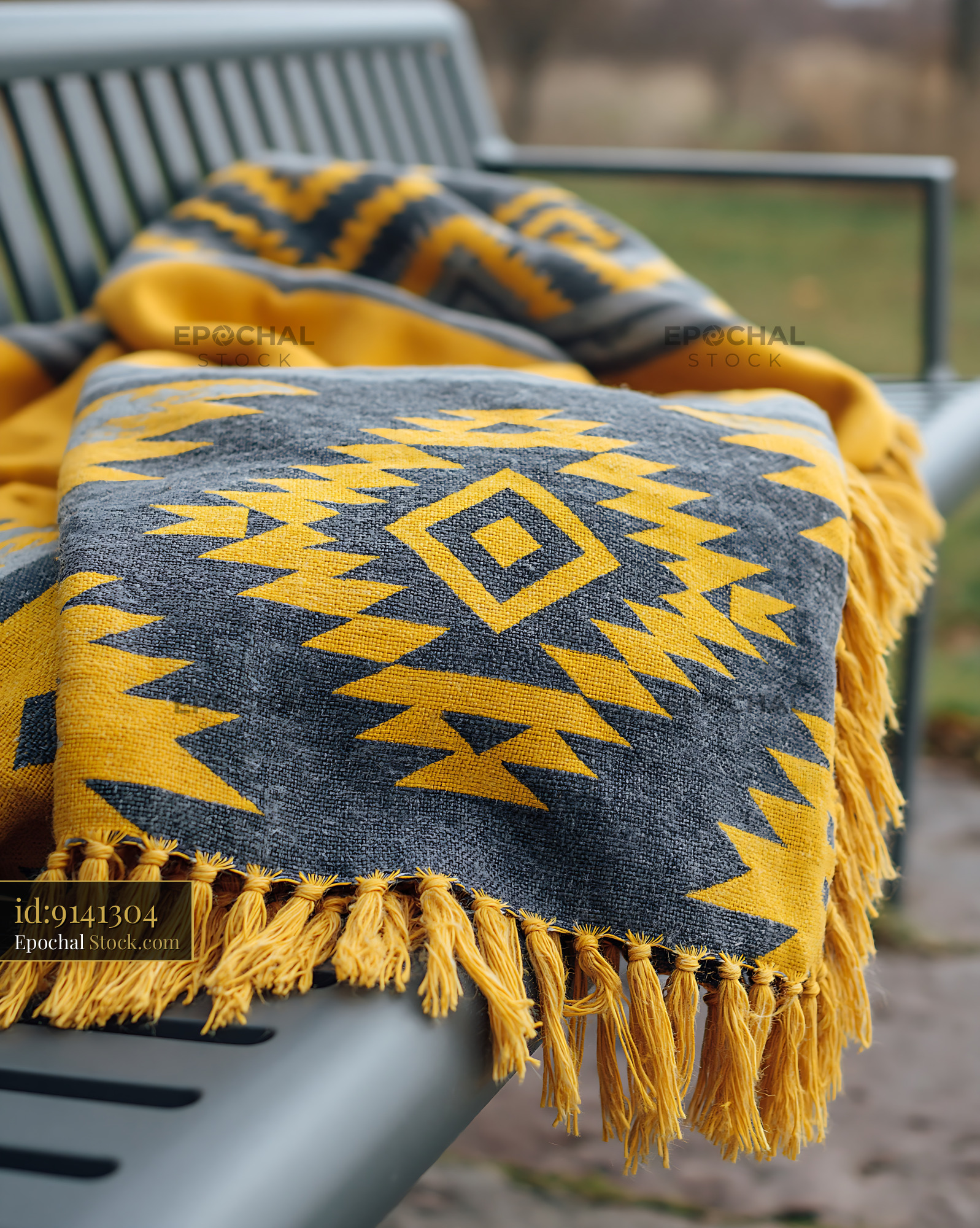 Patterned blanket with yellow geometric design on a metal park seat - stock photo