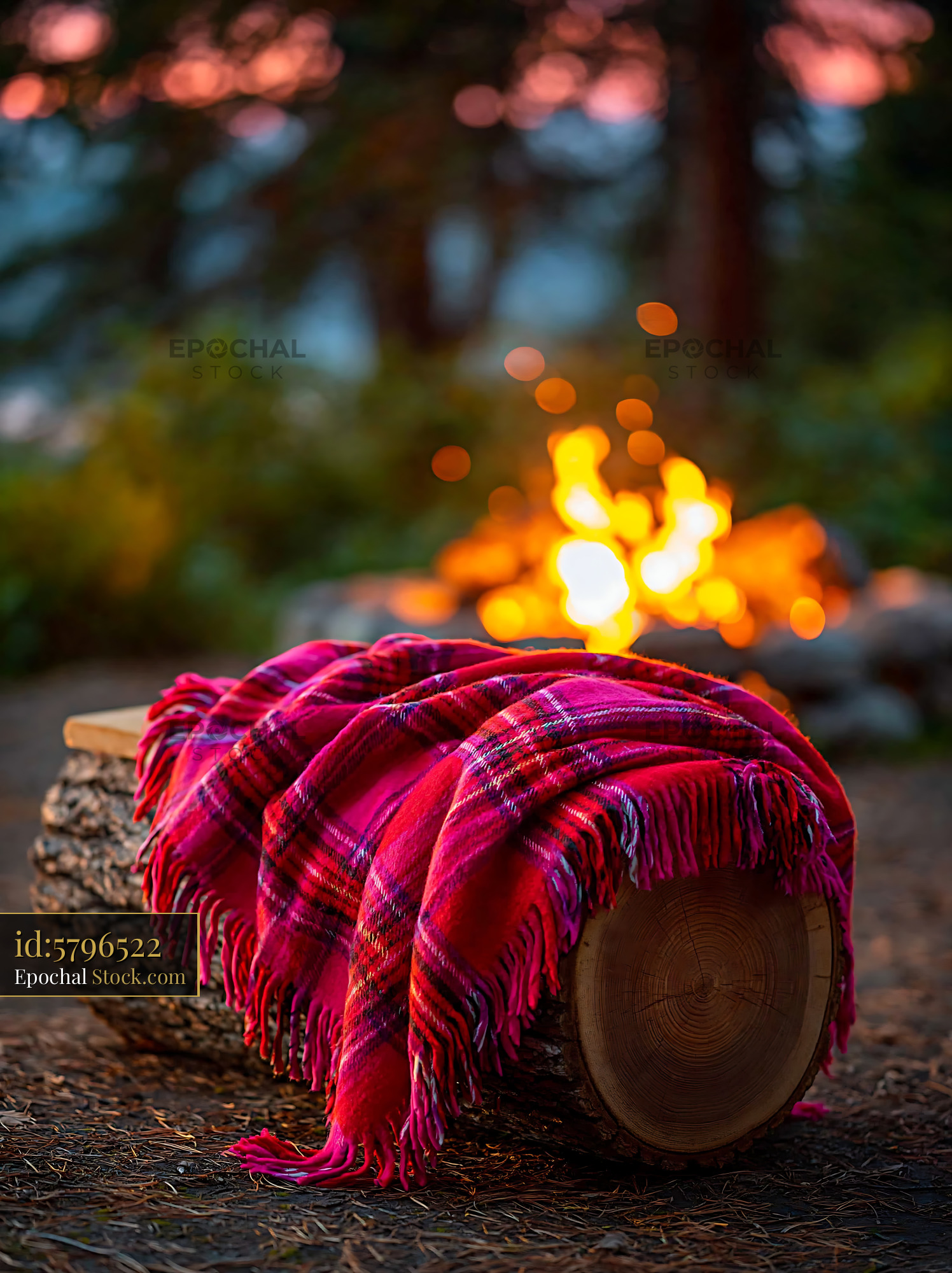 Cozy wooden seat with throw by a campfire at twilight - stock photo