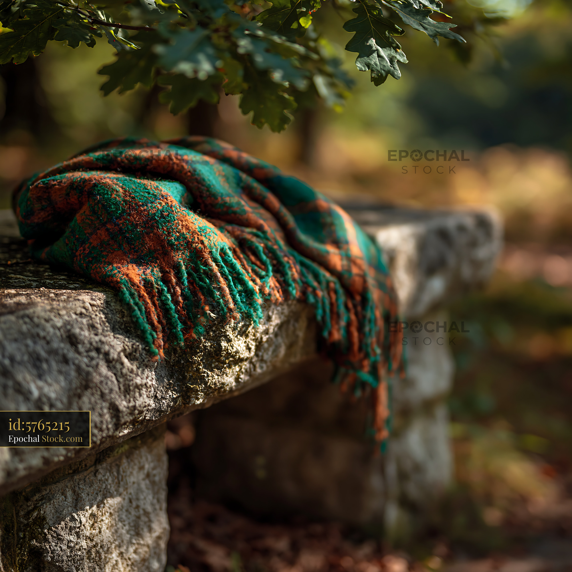 Cozy striped throw on stone bench under oak tree in autumn - stock photo