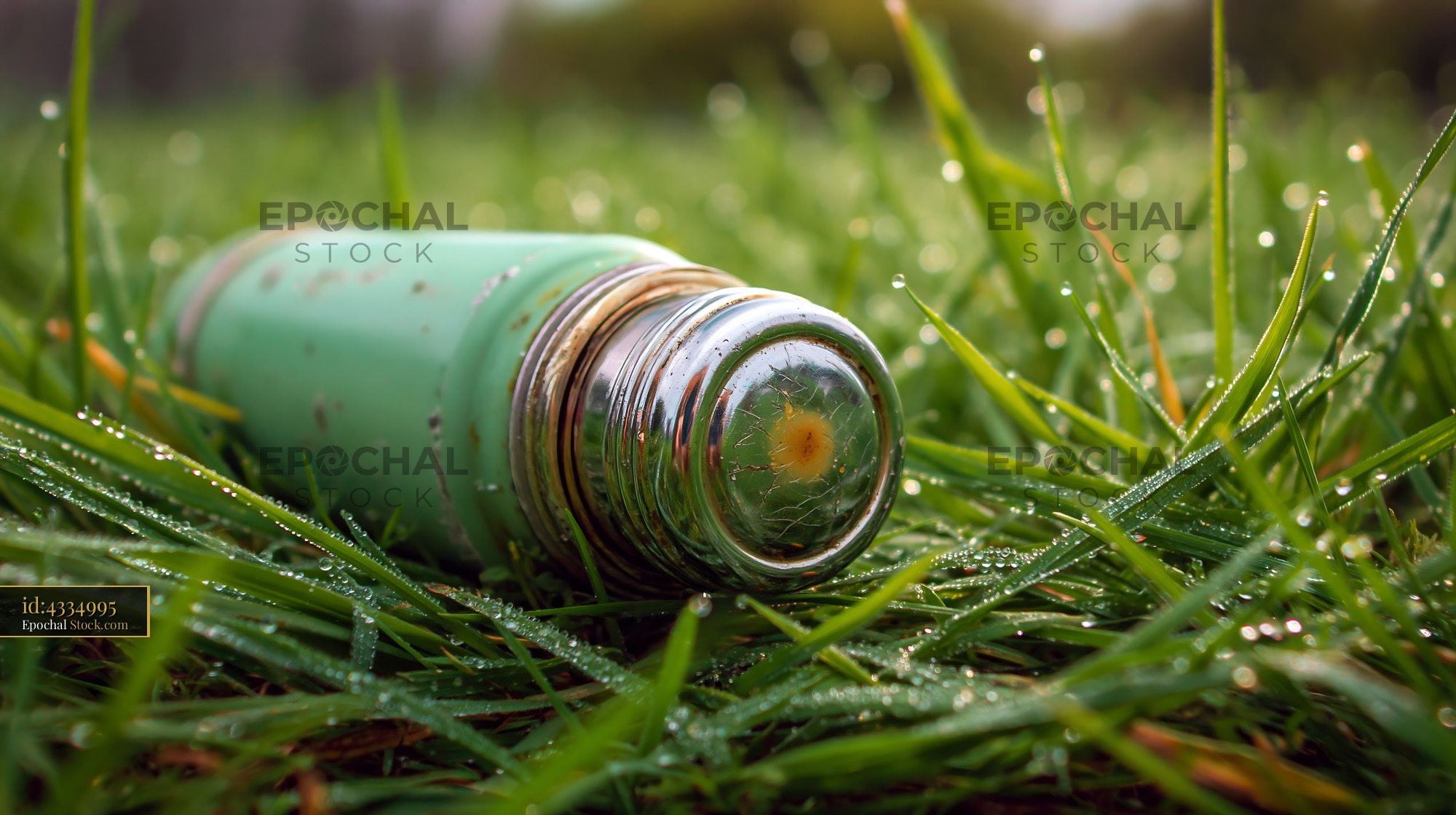 Green thermos lying in wet grass with morning dew at sunrise - stock photo