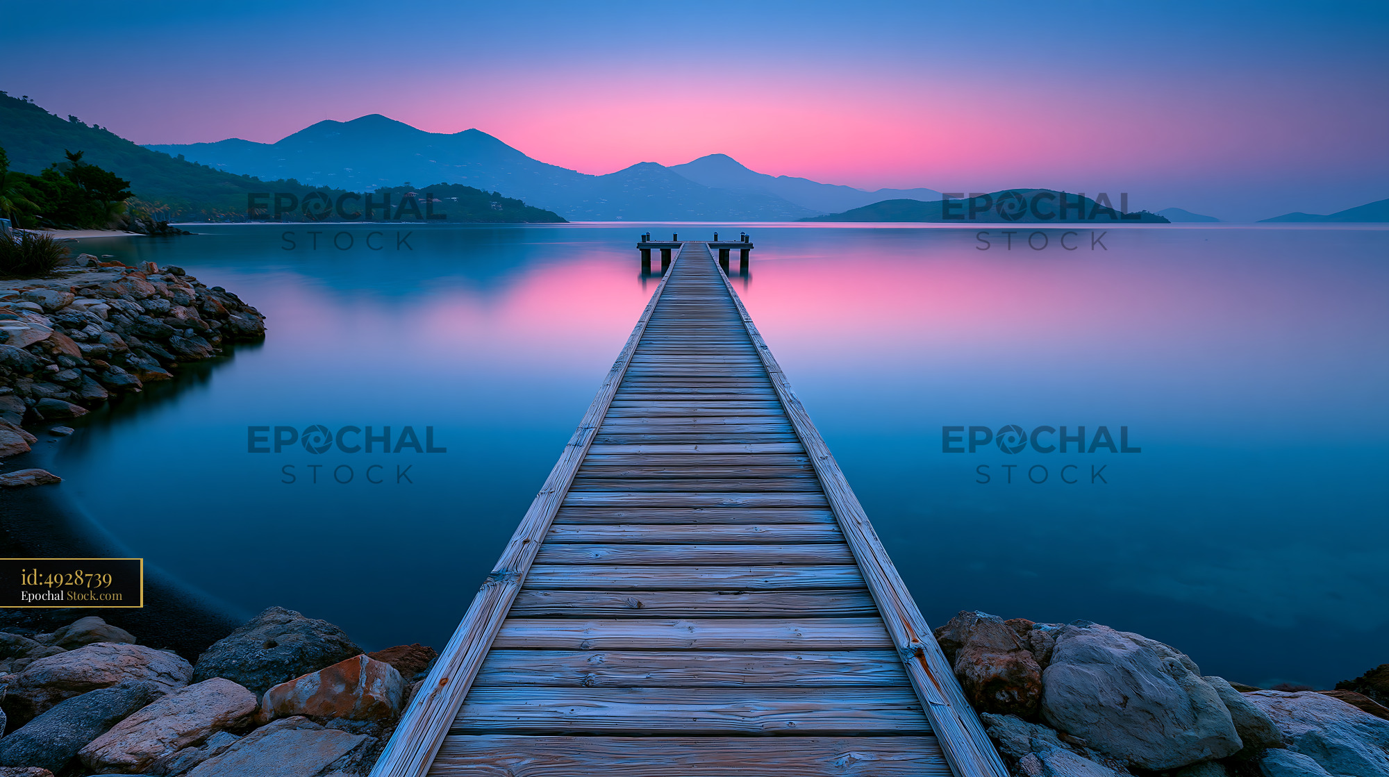 Wooden pier stretching into calm water during a vibrant pink sunset - stock photo