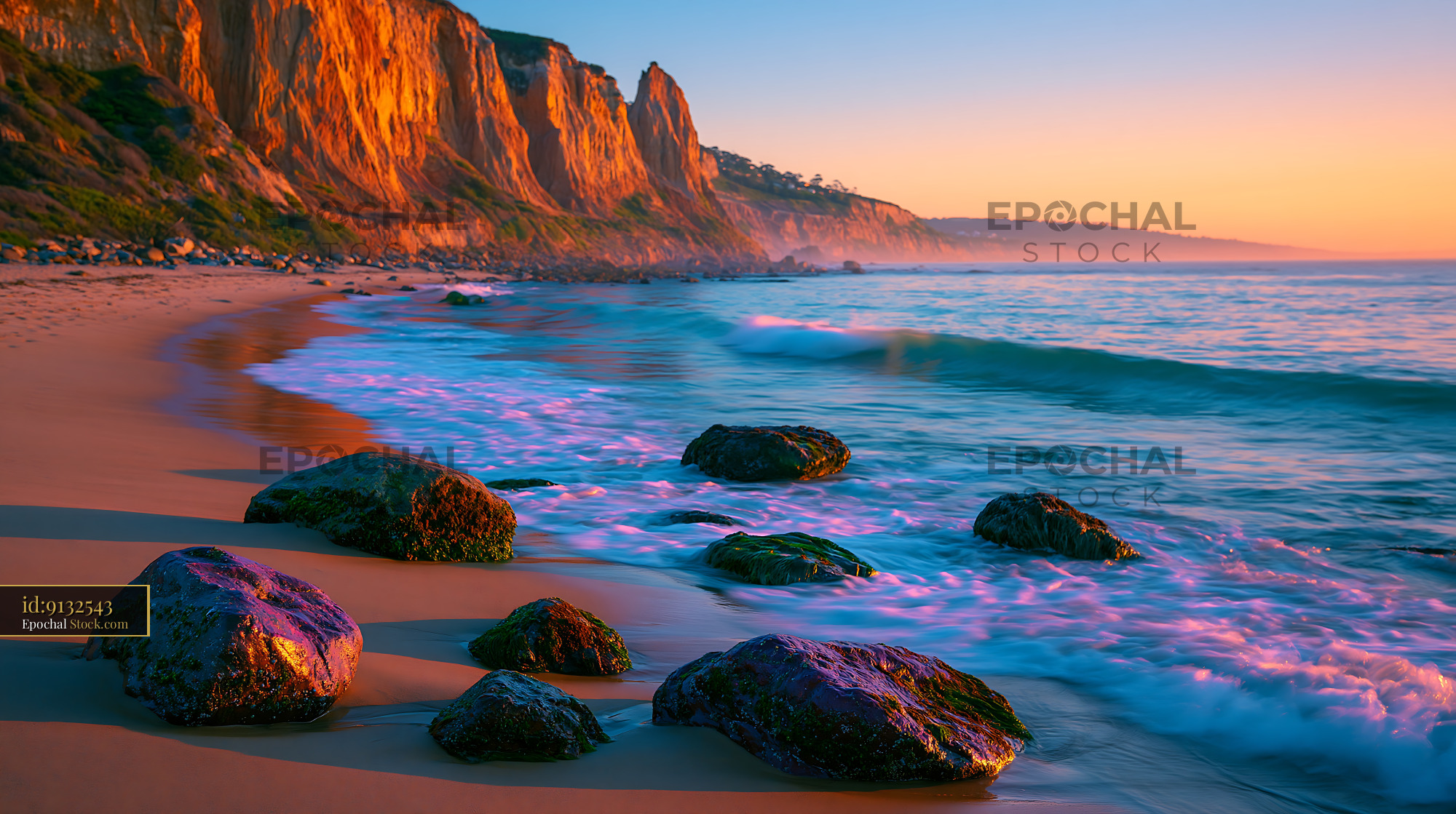 Golden sunset over a rocky beach with towering cliffs and ocean waves - stock photo