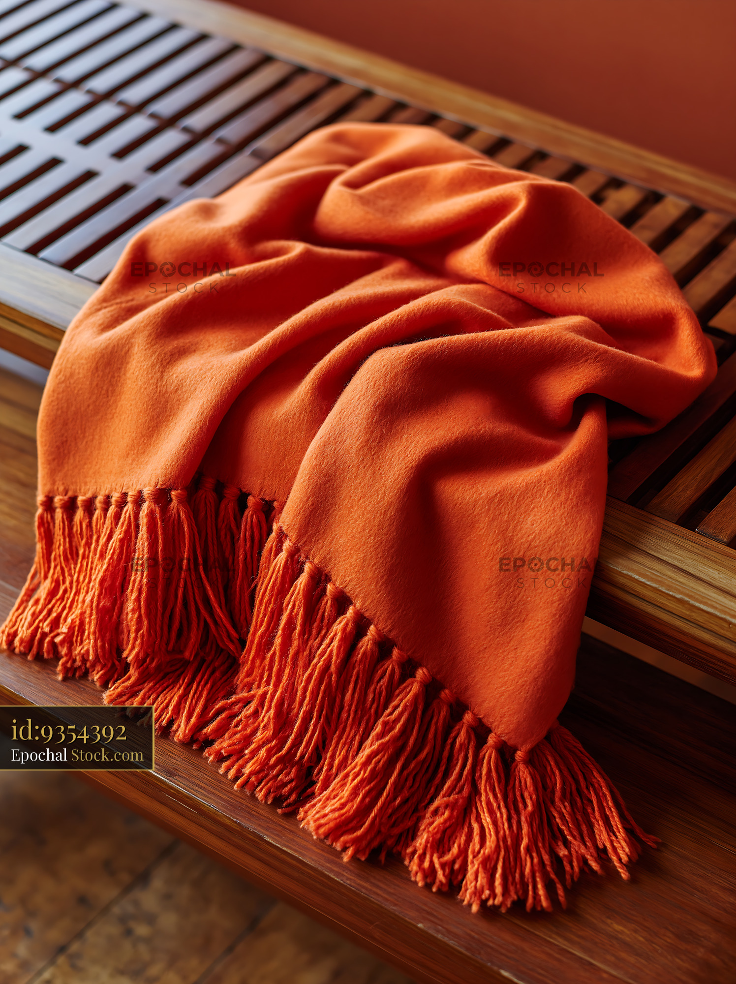 Soft orange cashmere throw with tassels draped on a wooden bench - stock photo
