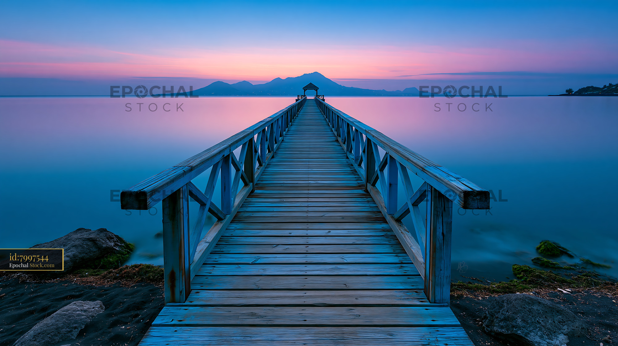 Long wooden pier leading to a pavilion at sunset with mountain view - stock photo