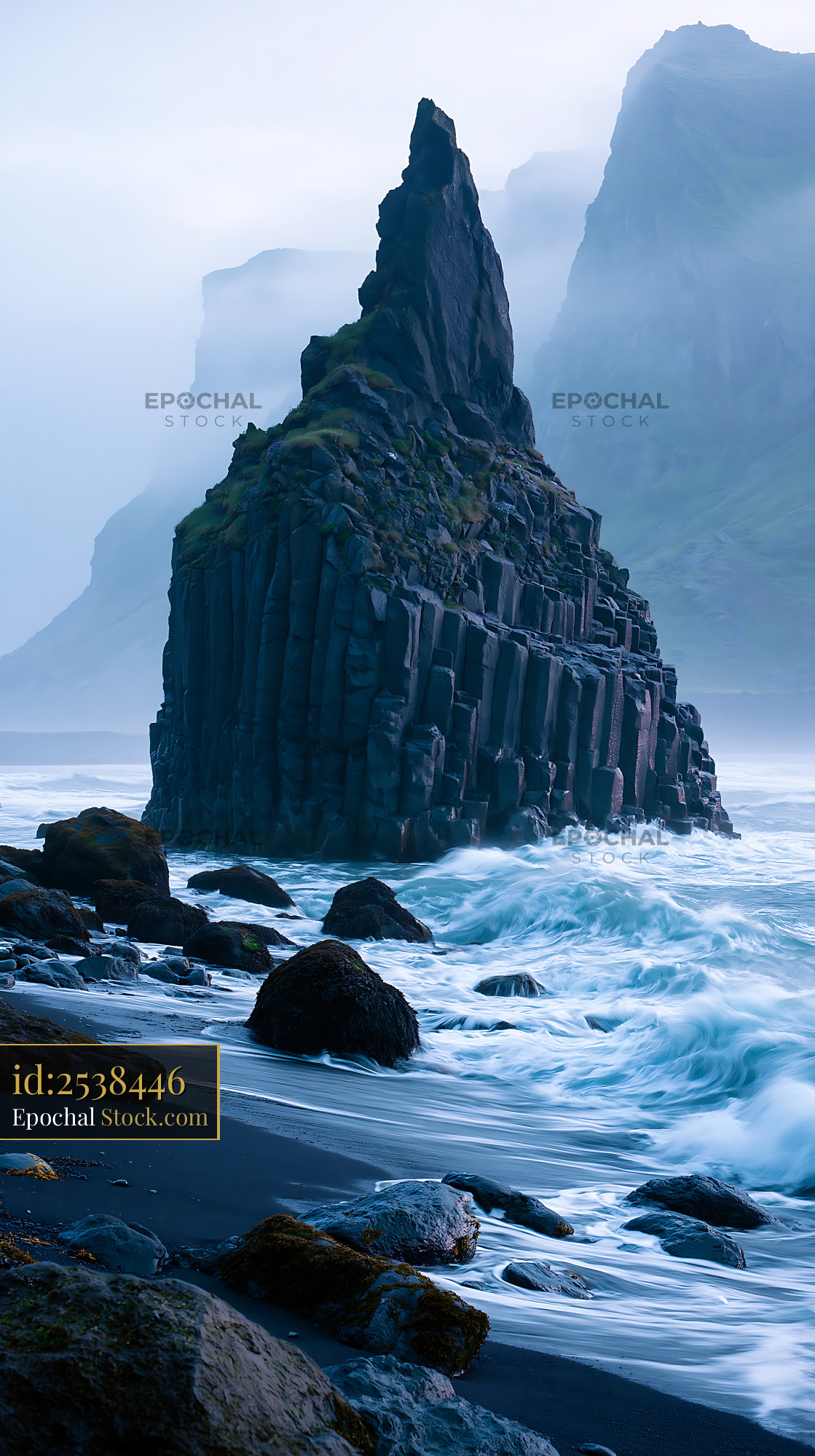 Basalt sea stack on a black sand beach with crashing waves in the mist - stock photo