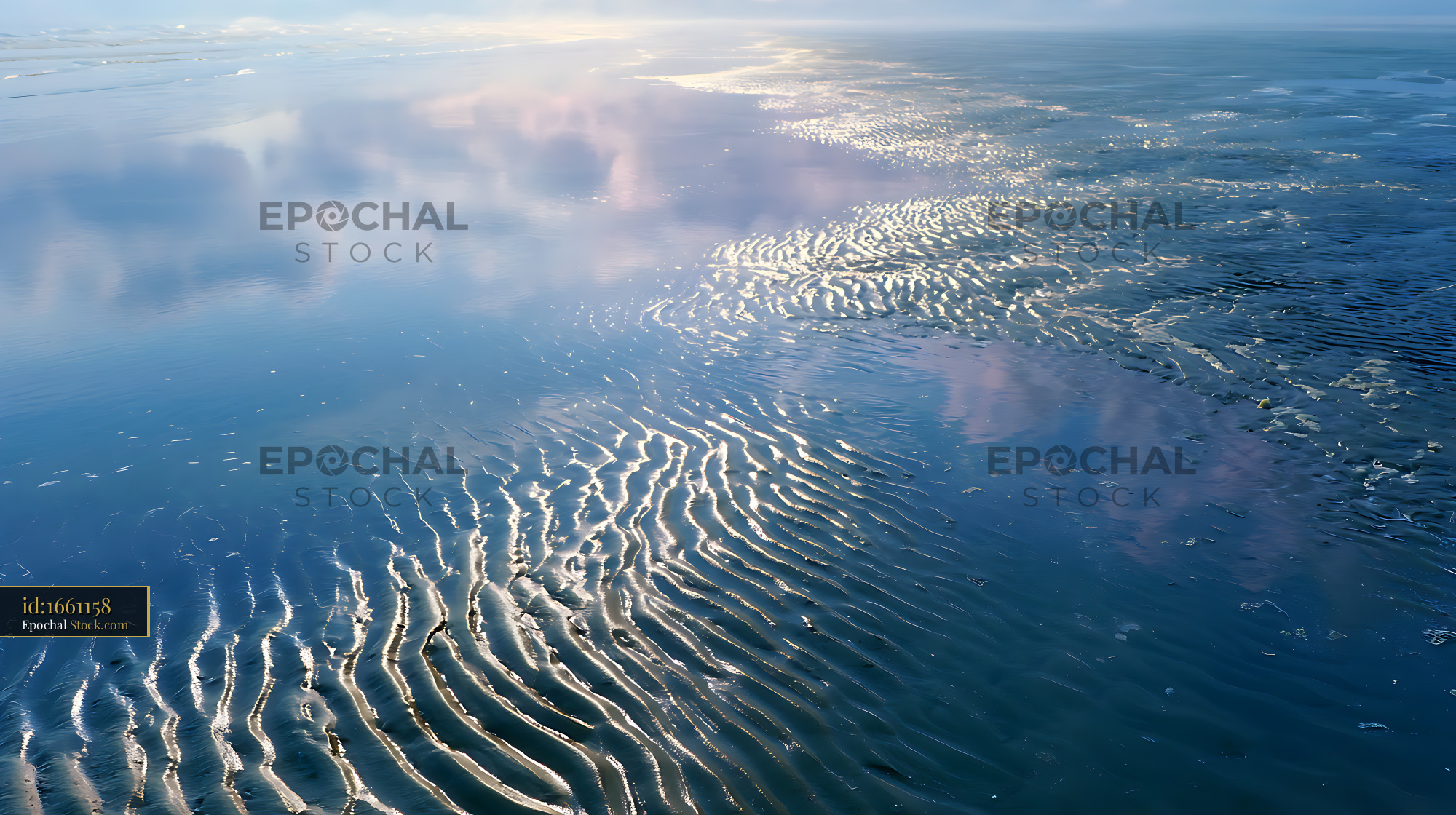 Sand ripples on a tidal mud flat reflecting the soft blue sky - stock photo